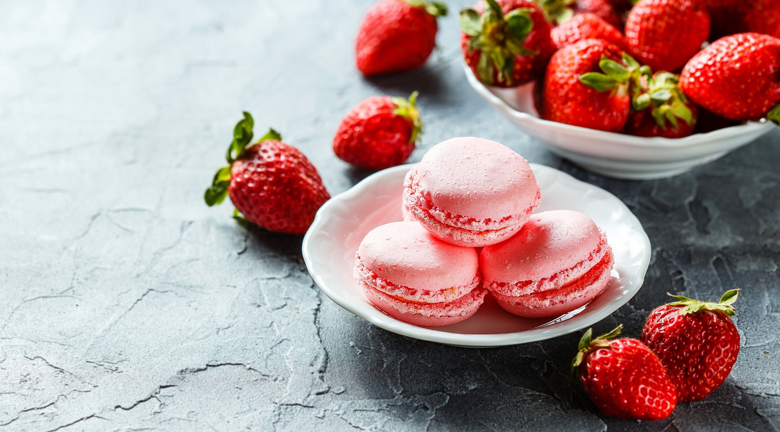 Pink macarons and fresh strawberries on a textured surface HD Wallpaper
