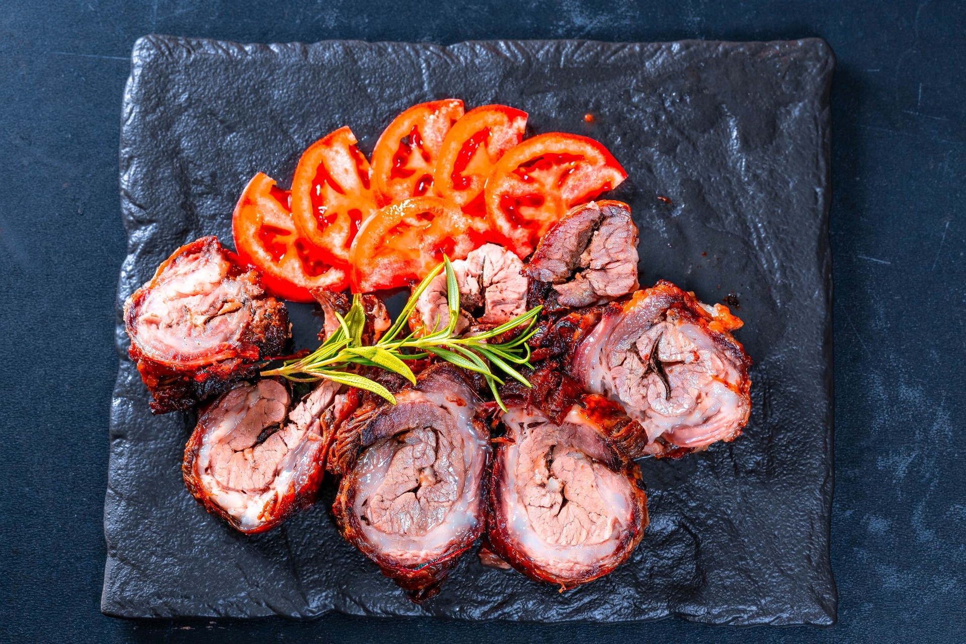 Sliced meat with tomatoes and rosemary on a slate plate HD Wallpaper