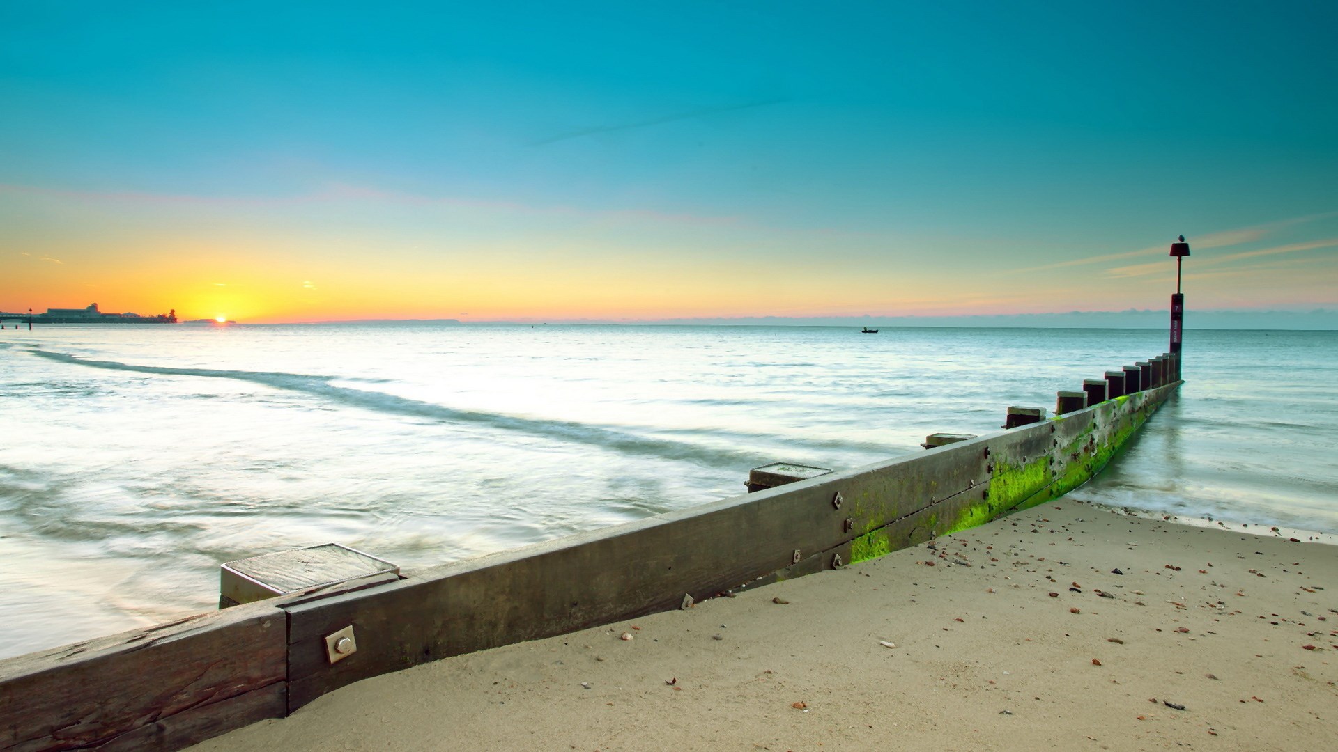 Beach sunrise with wooden breakwater and distant ship HD Wallpaper