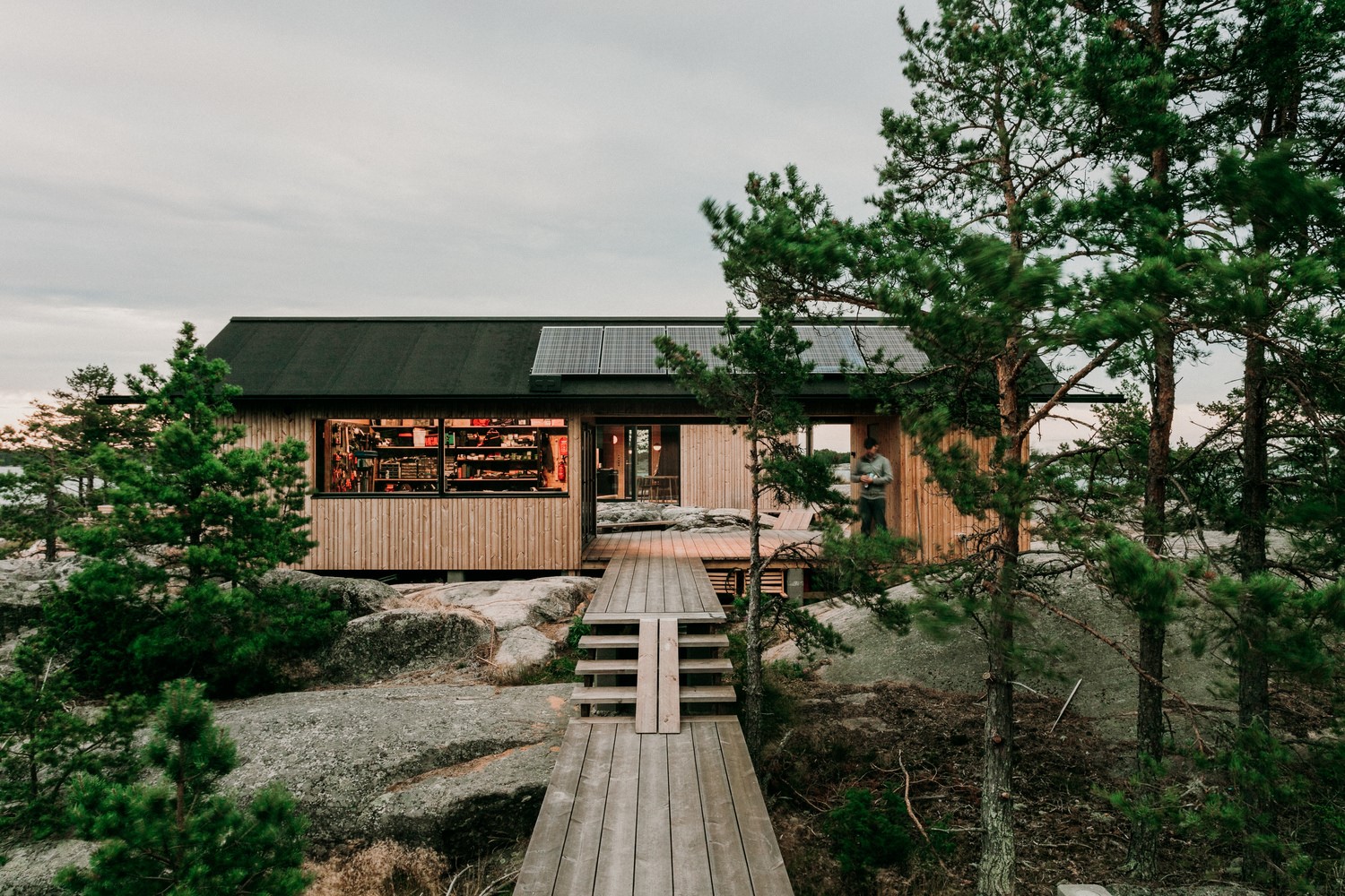 Modern wooden cabin with solar panels in a rocky, forested landscape HD Wallpaper