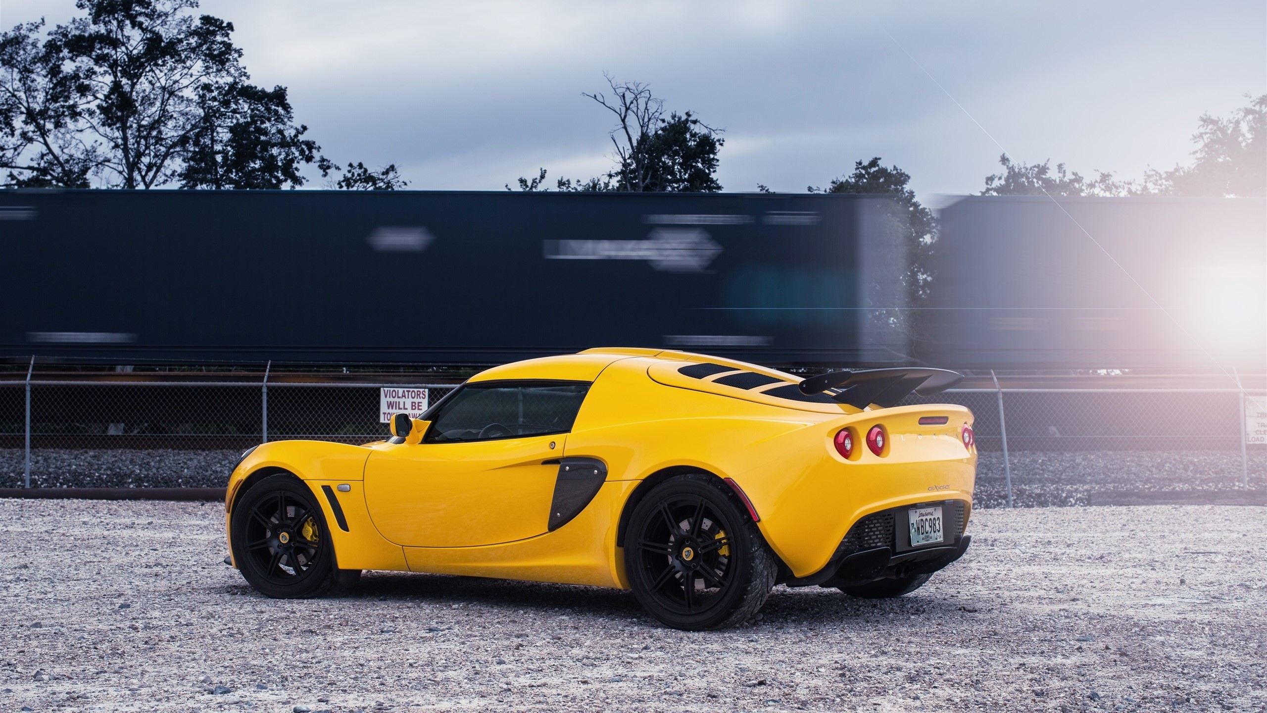 Yellow Lotus car parked near a moving train HD Wallpaper