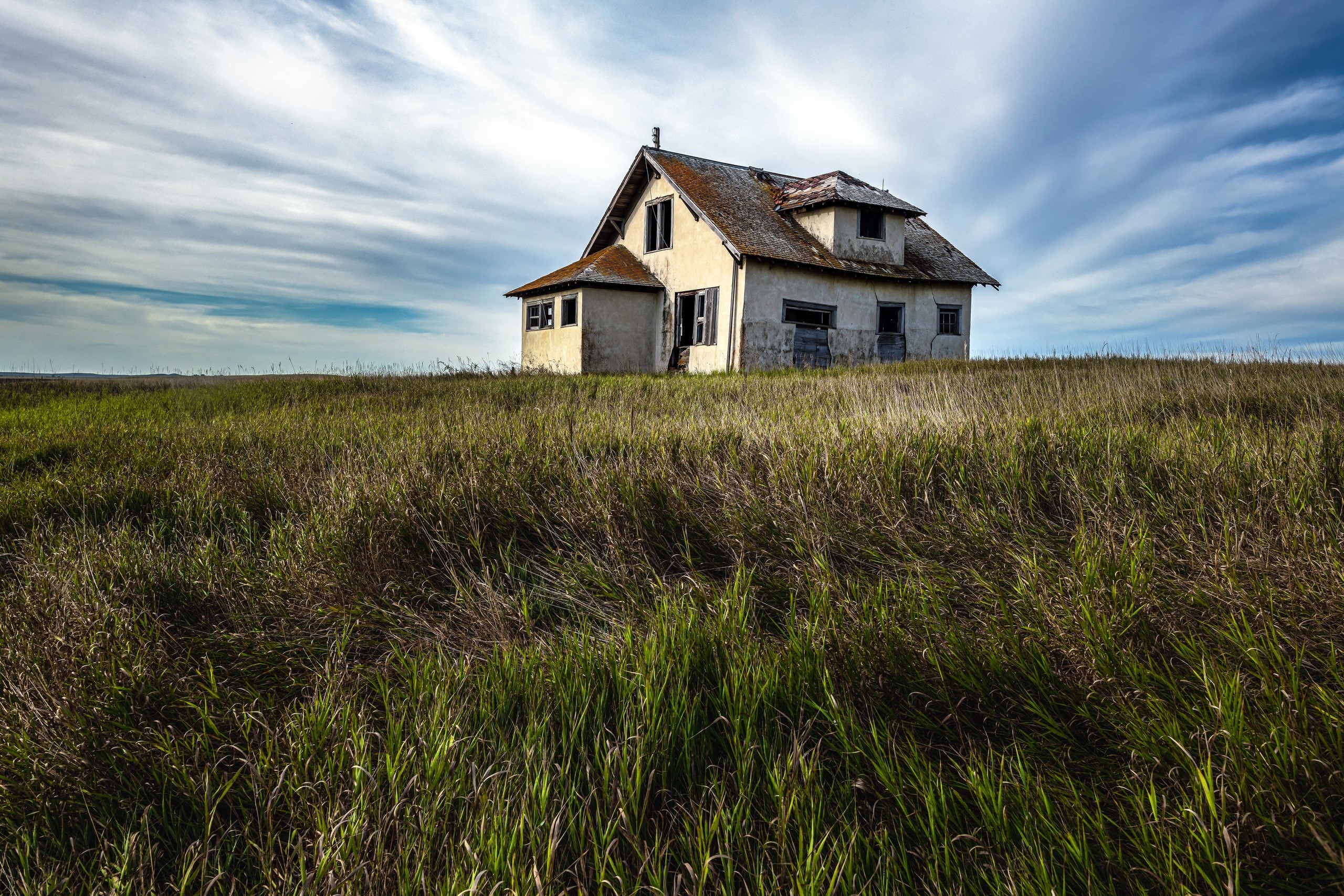 Abandoned house in a grassy field under a cloudy sky HD Wallpaper