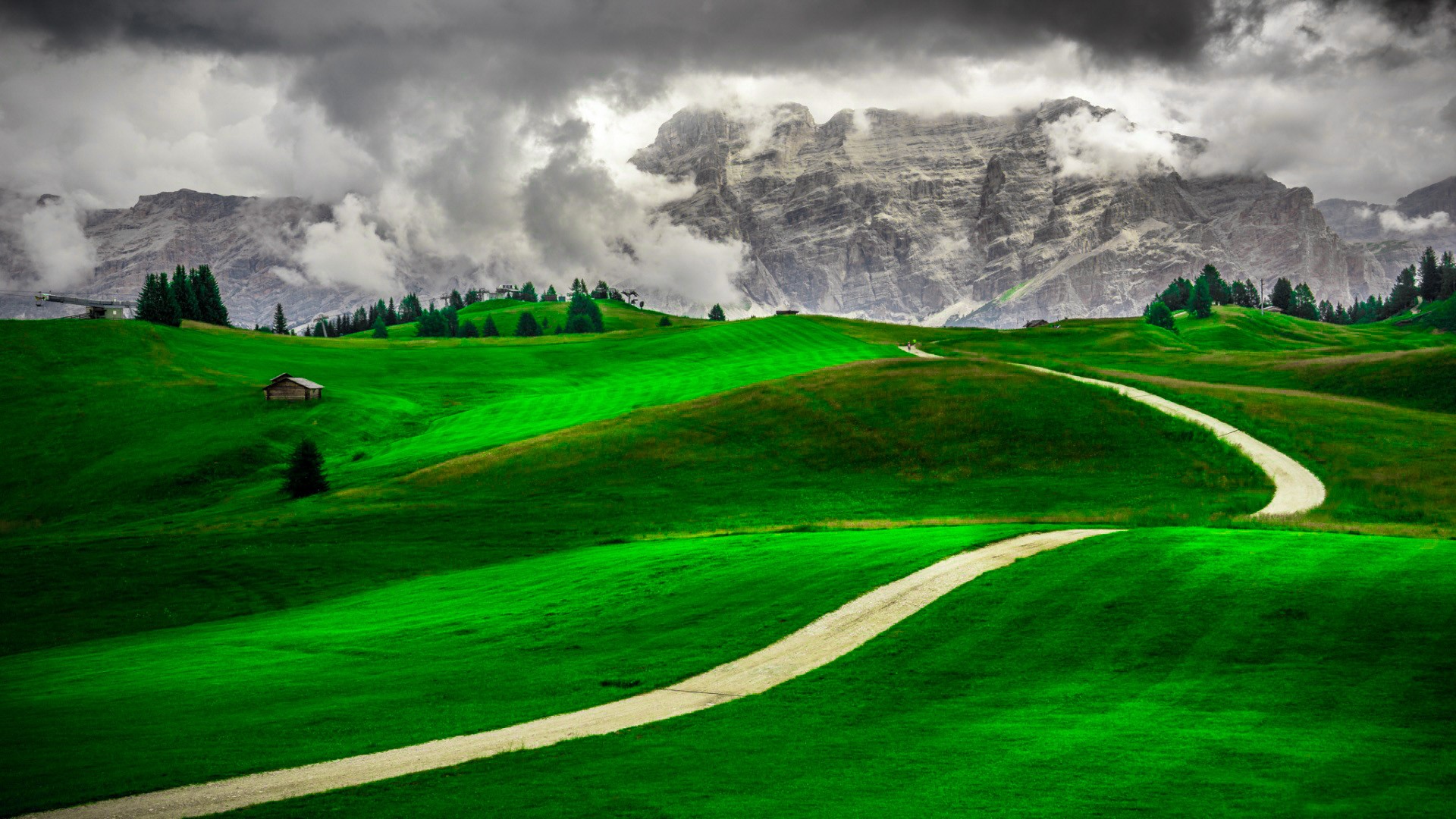 Winding road through green hills towards cloudy mountains HD Wallpaper