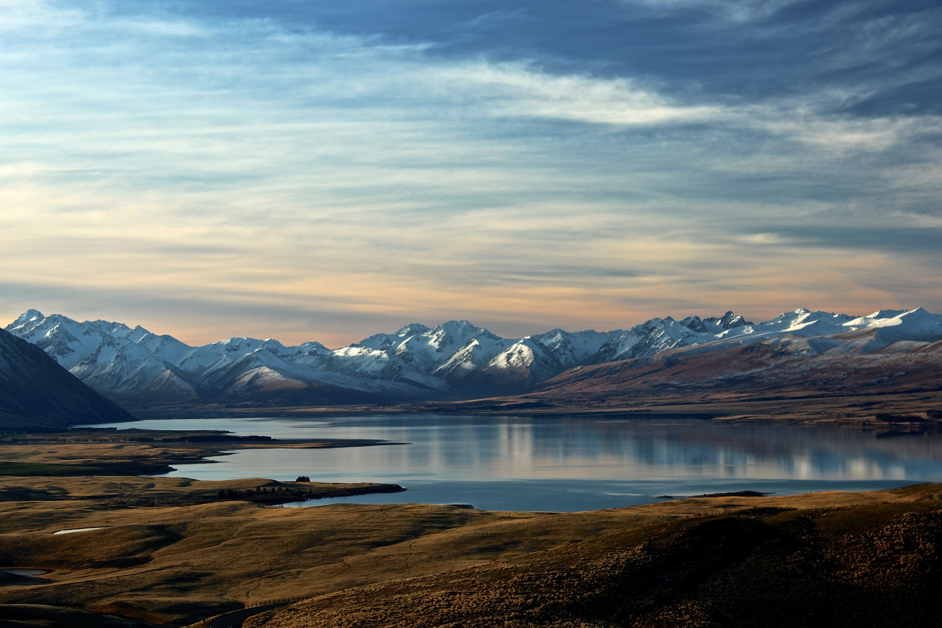 Snow-capped mountains reflected in a calm lake with rolling hills HD Wallpaper
