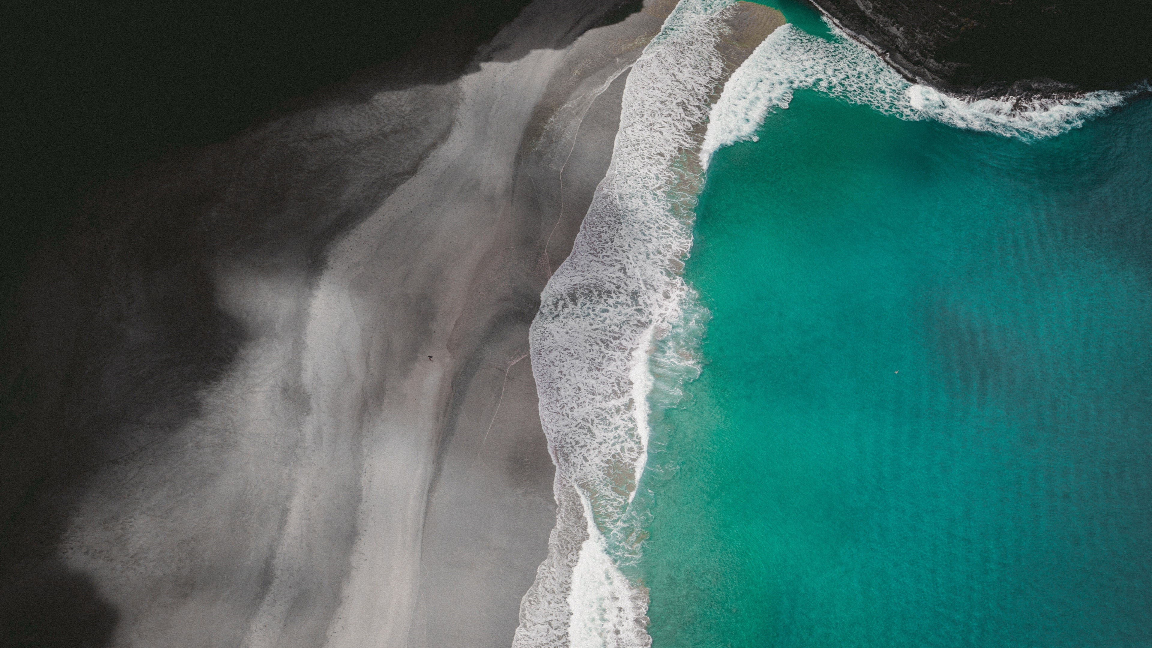 Aerial view of a dark sand beach with turquoise waves HD Wallpaper