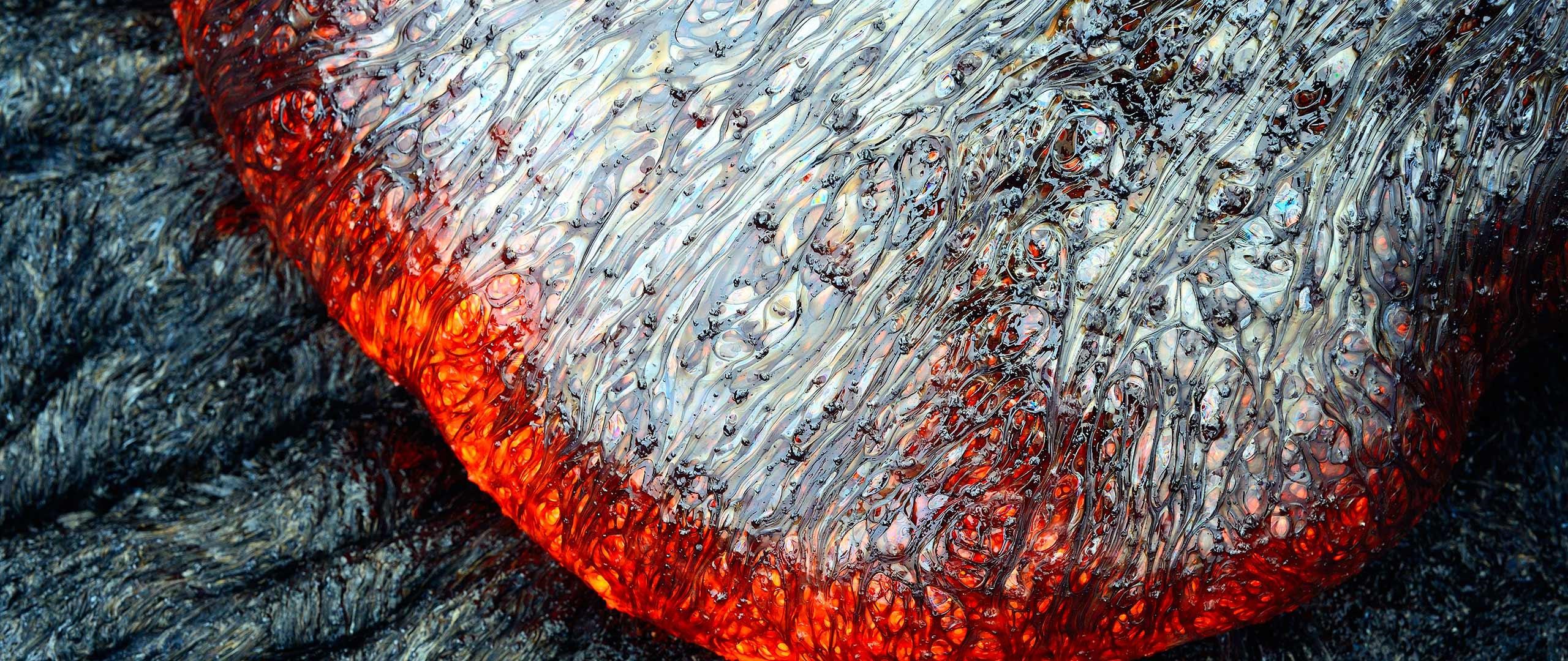 Close-up of molten lava flowing over dark rock HD Wallpaper