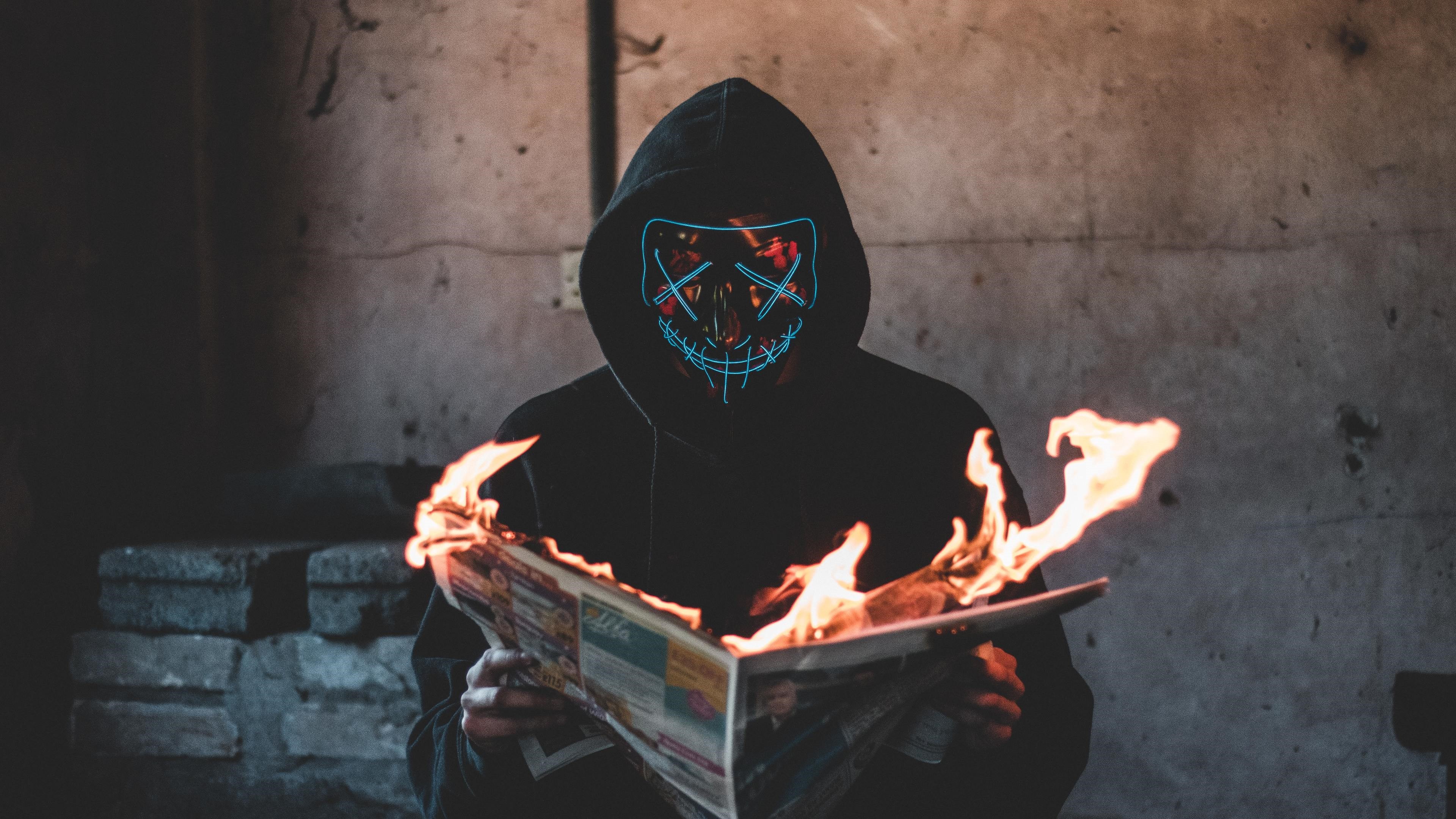 Person in neon mask burning newspaper HD Wallpaper