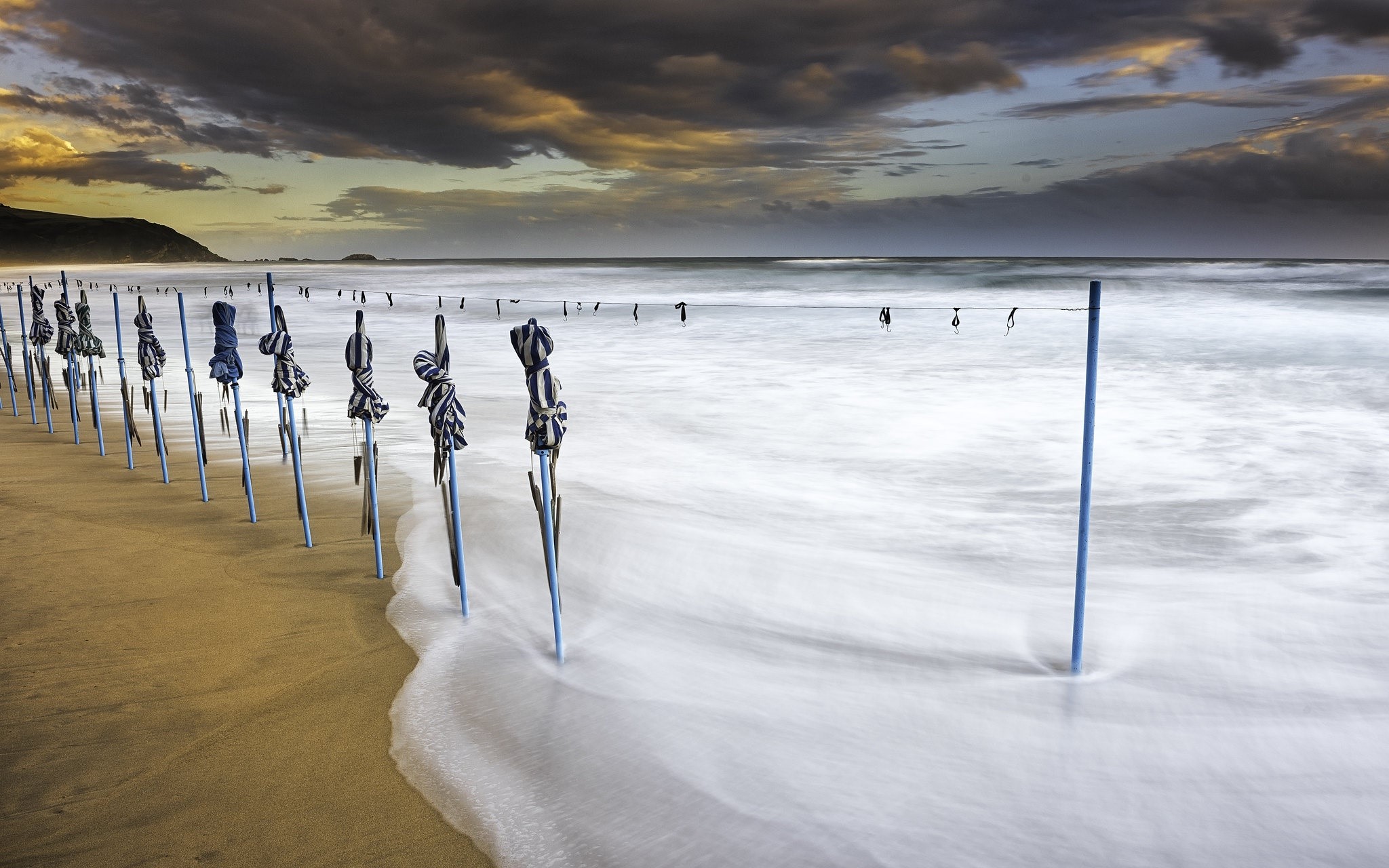 Beach with closed umbrellas and ocean waves HD Wallpaper