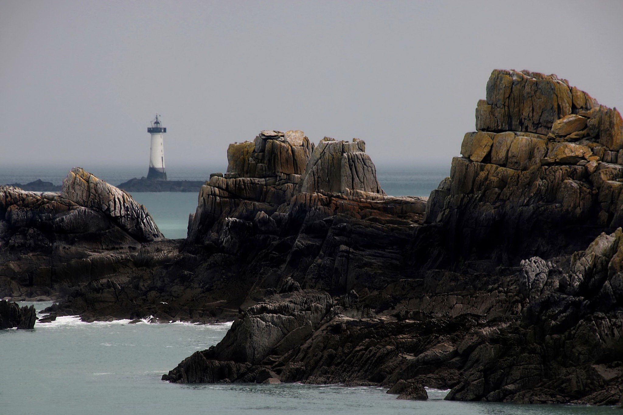 Rocky coast with a lighthouse in the distance HD Wallpaper