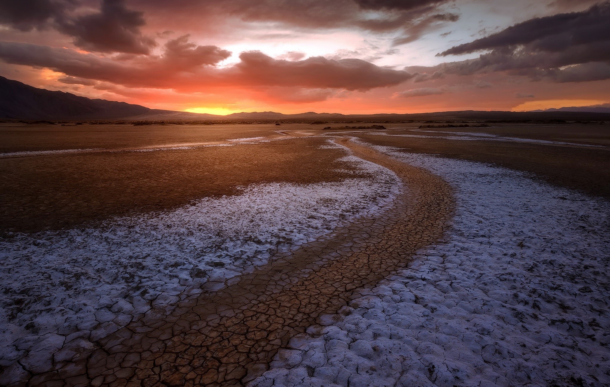 Desert landscape at sunset with cracked earth and mountains HD Wallpaper