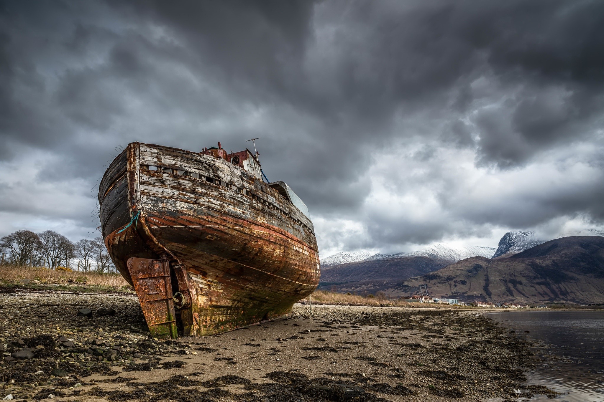 Abandoned wooden shipwreck on a muddy shore under stormy clouds HD Wallpaper
