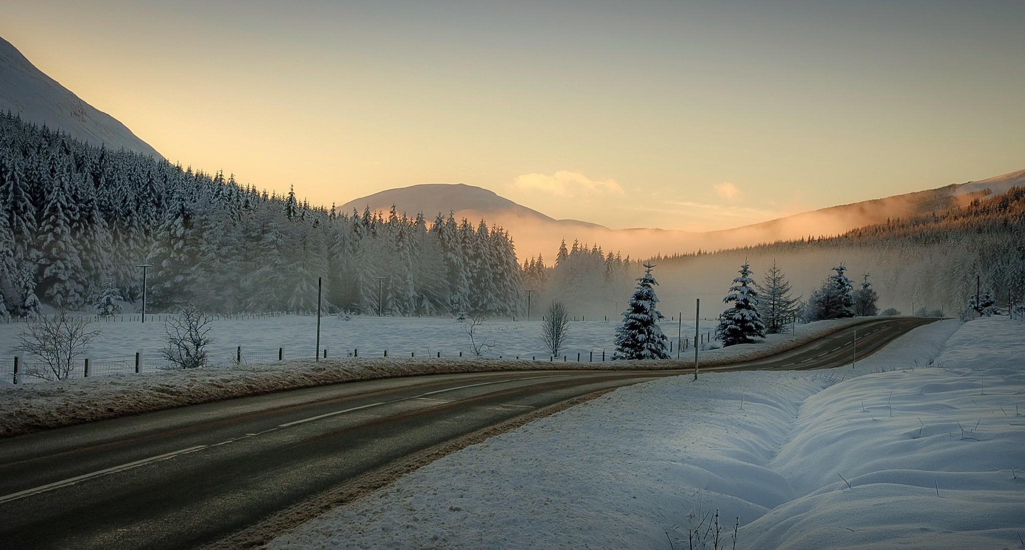 Winter road through snow-covered forest and mountains at sunrise HD Wallpaper