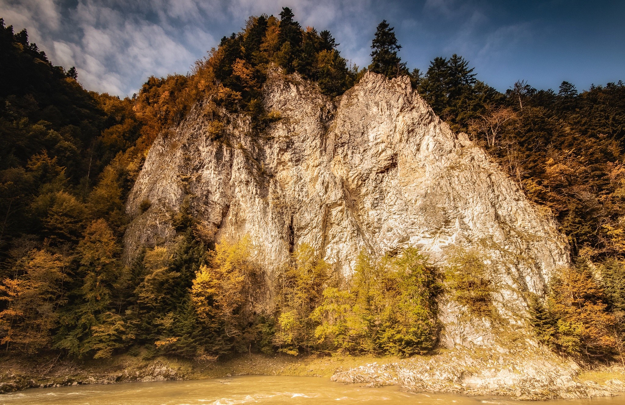 Rocky cliff face with autumn trees and river HD Wallpaper