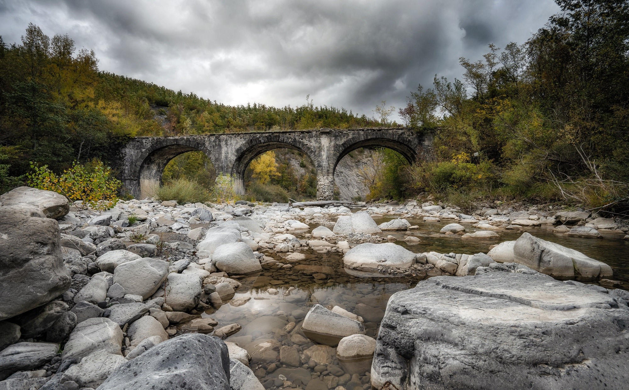 Stone bridge over a rocky riverbed in Emilia-Romagna, Italy HD Wallpaper