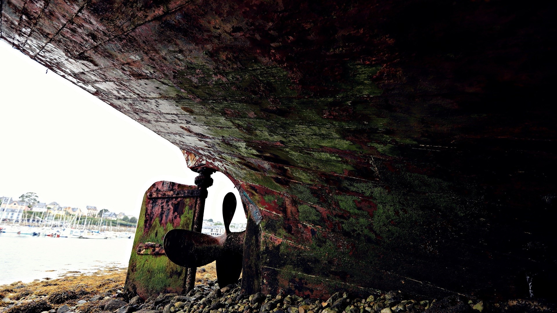 Old shipwreck propeller on rocky shore HD Wallpaper