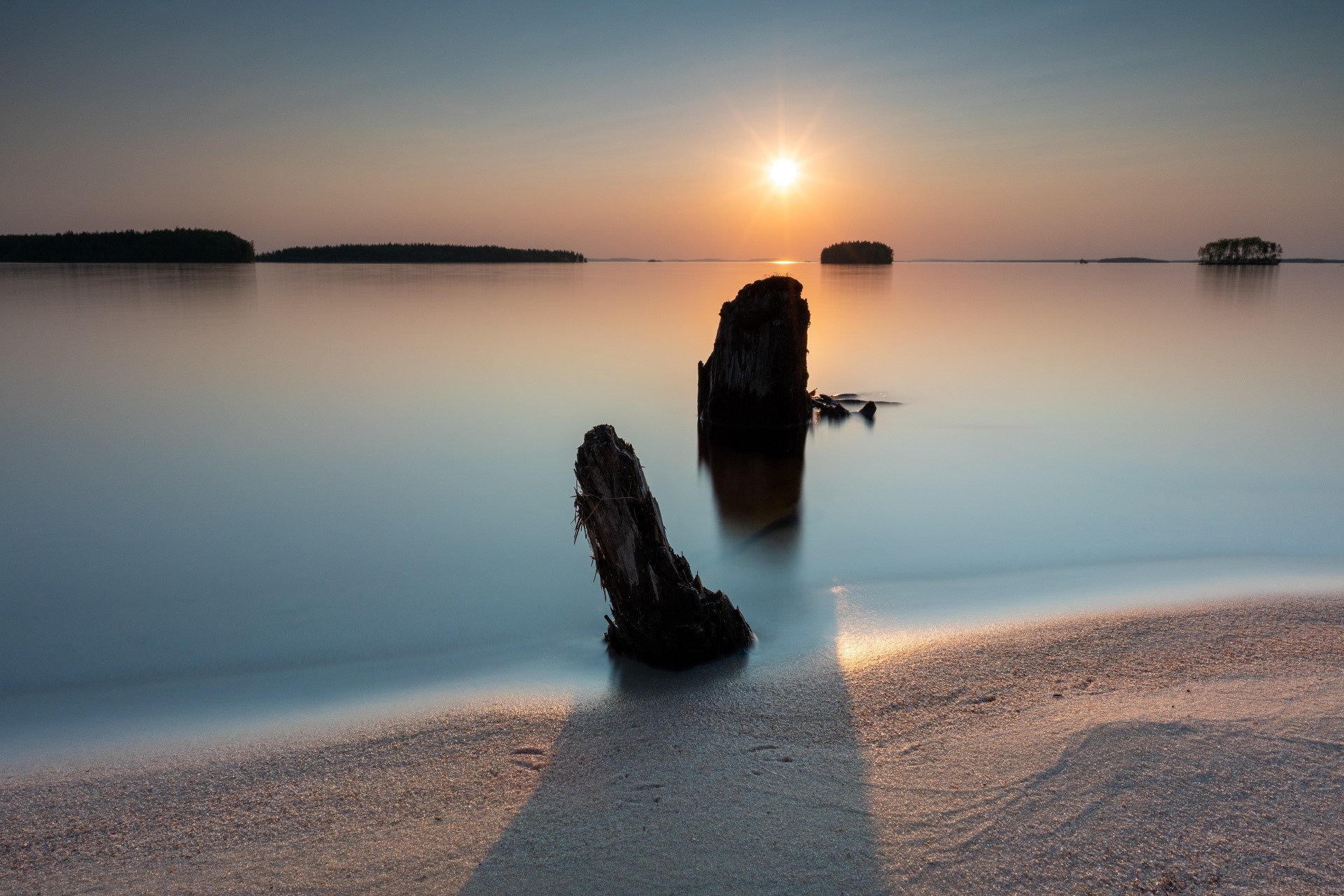 Sunset over calm water with wooden posts on beach HD Wallpaper