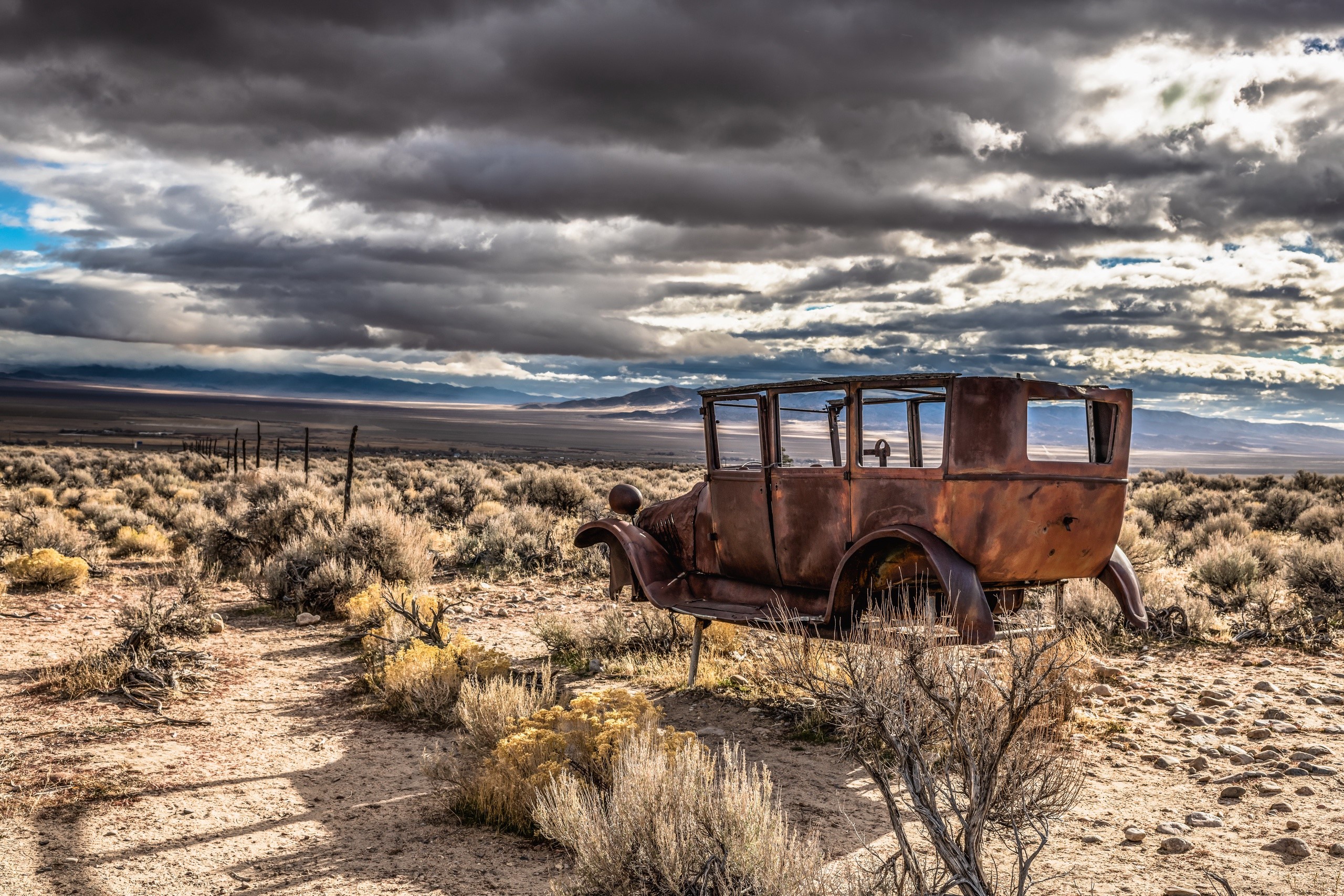 Rusty vintage car in a desolate landscape under stormy clouds HD Wallpaper