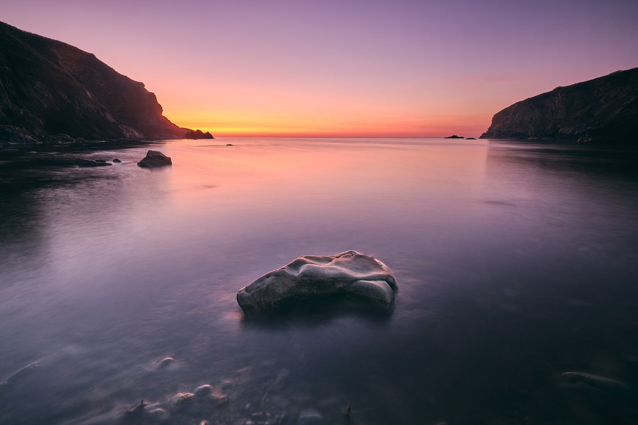 Coastal landscape at sunset with calm water and rocks HD Wallpaper