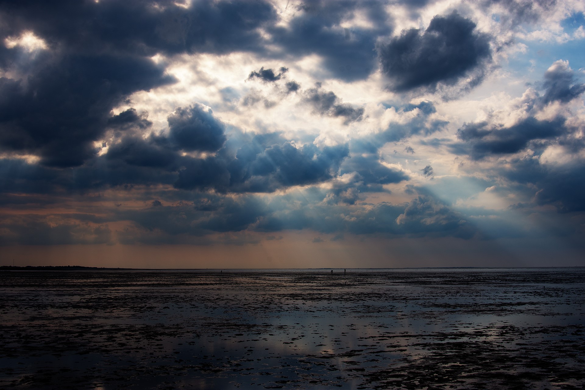Sun rays breaking through dramatic clouds over a tidal flat HD Wallpaper