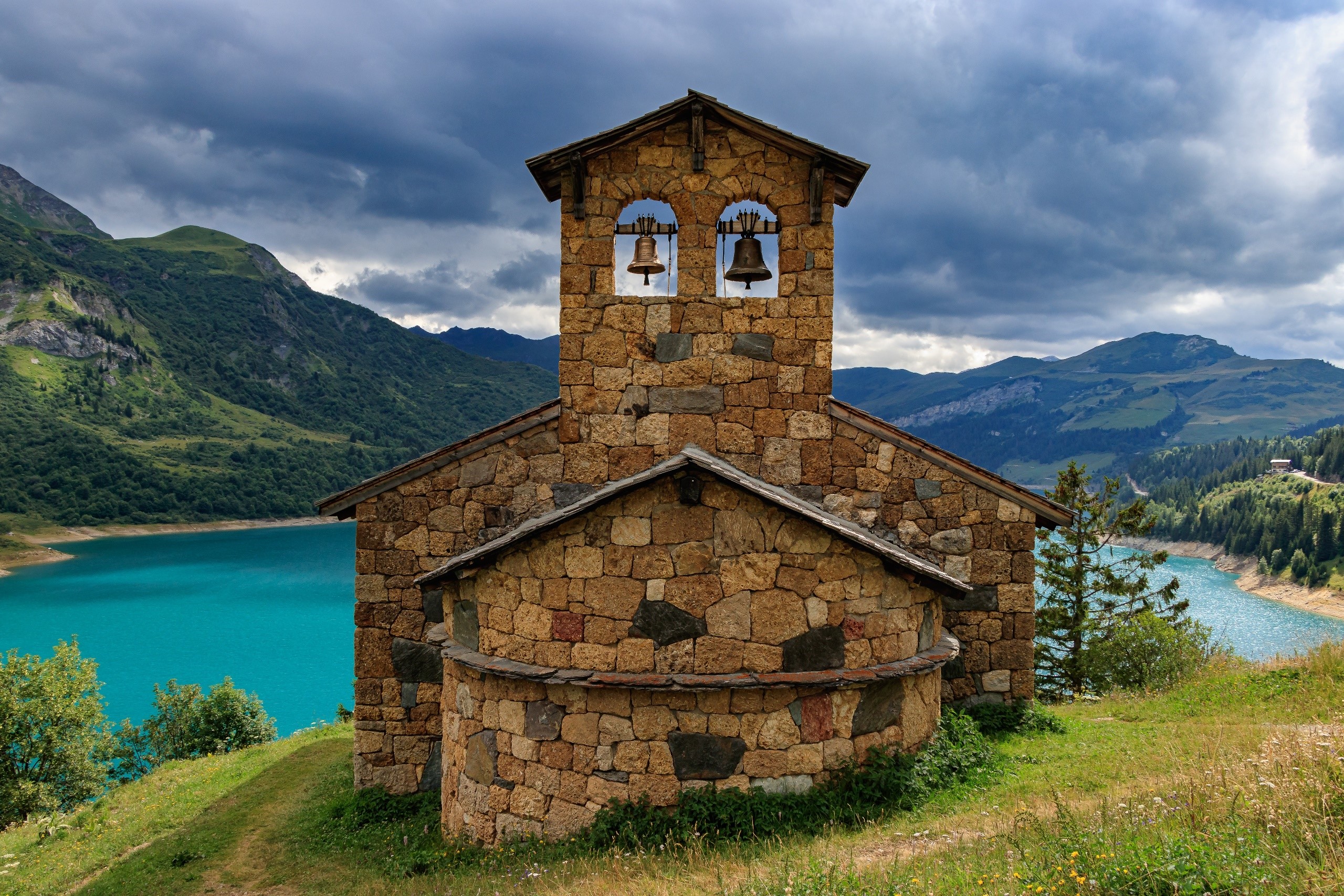 Stone church with bells by a turquoise lake in France HD Wallpaper