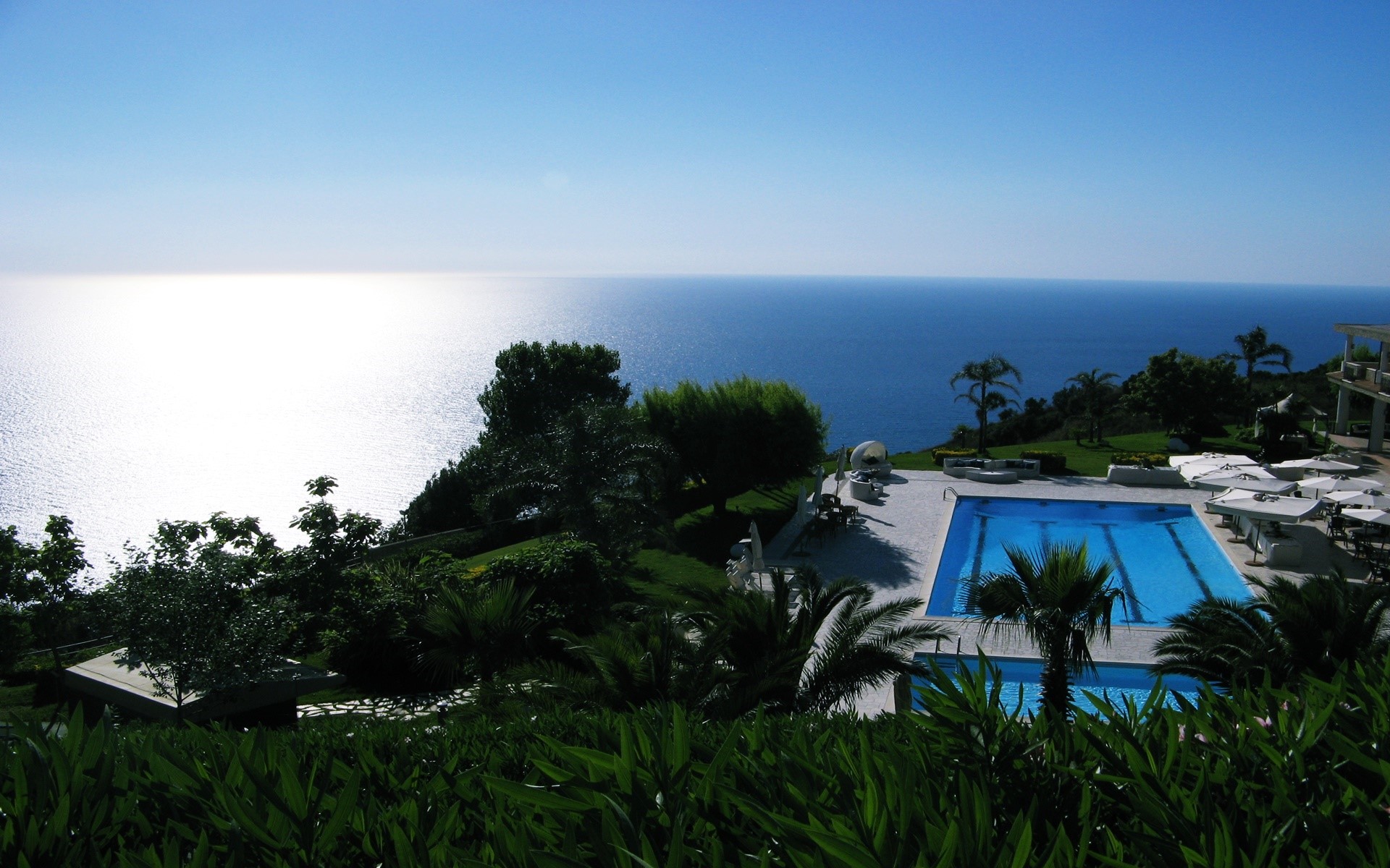 Resort swimming pool overlooking the sea with trees HD Wallpaper