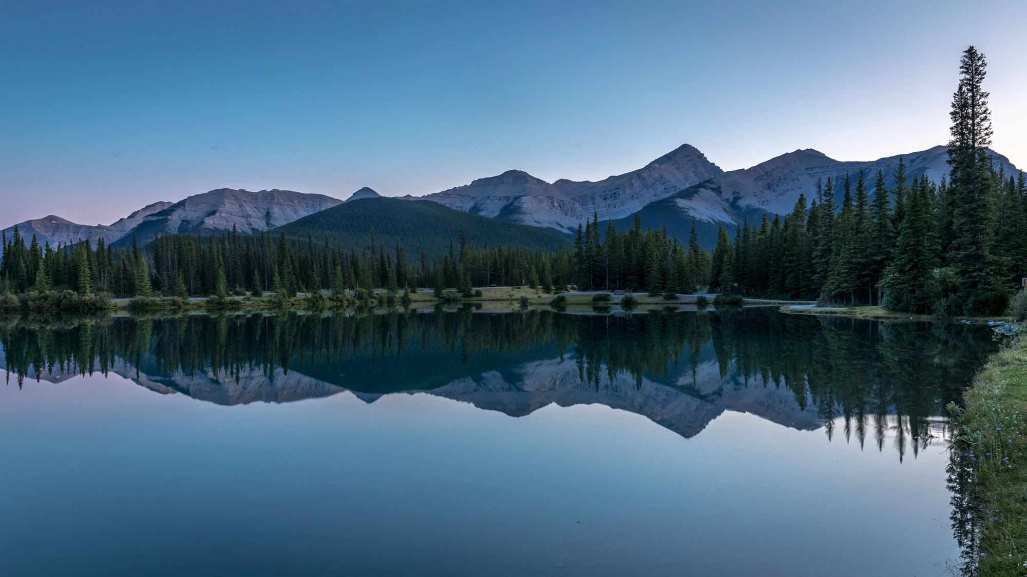 Mountains and trees reflected in a calm lake at dusk HD Wallpaper