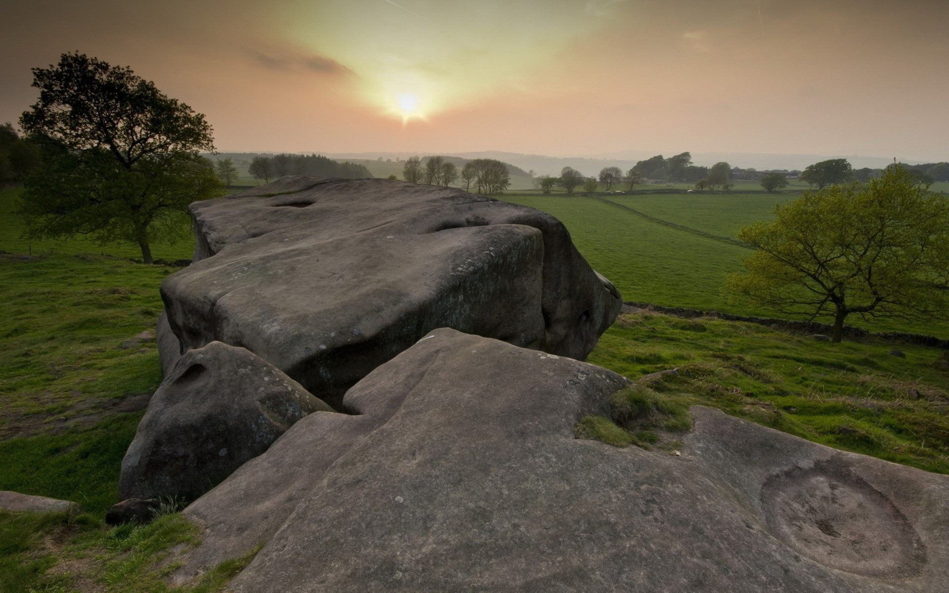 Rocky outcrop overlooking a green landscape at sunset HD Wallpaper