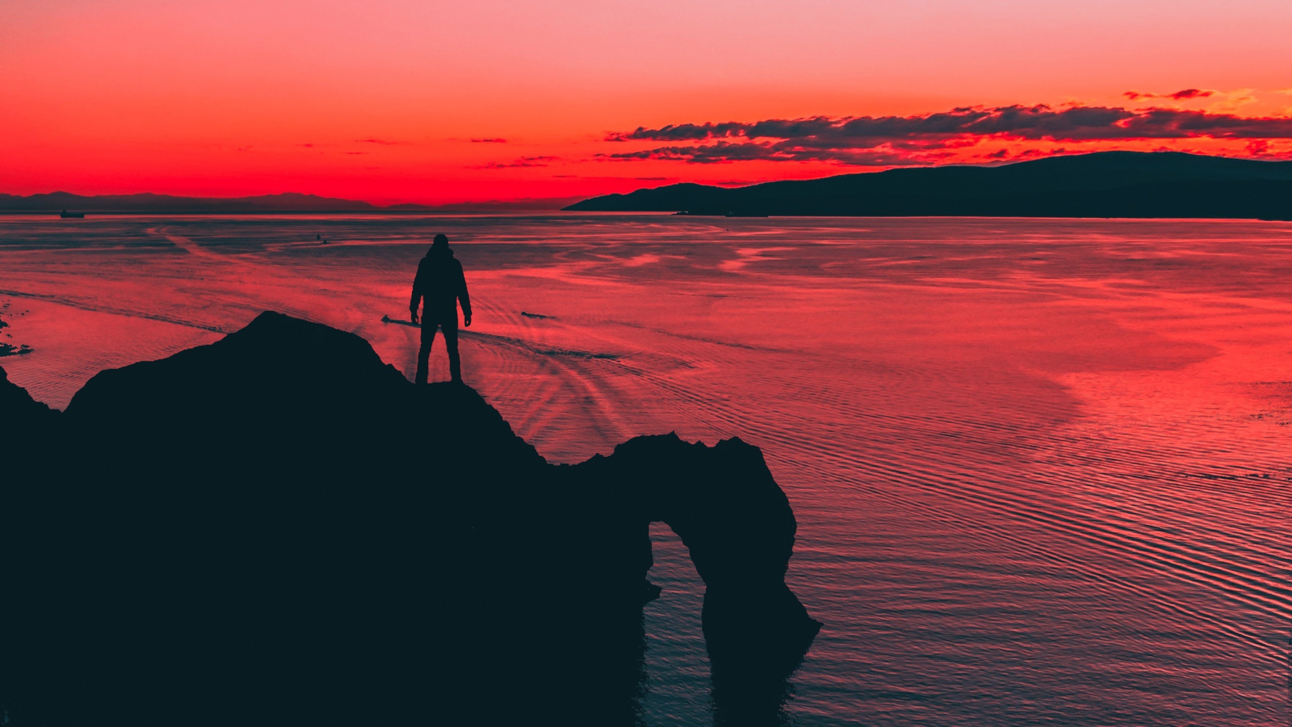 Man silhouetted on cliff overlooking ocean at sunset HD Wallpaper