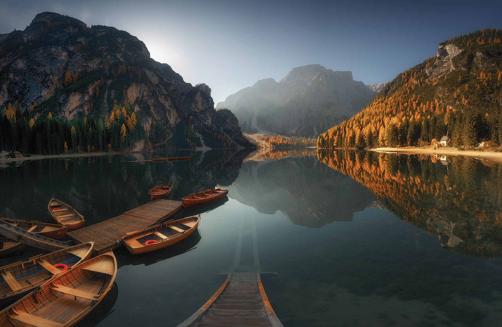 Wooden boats docked on a calm lake with mountains and autumn trees HD Wallpaper