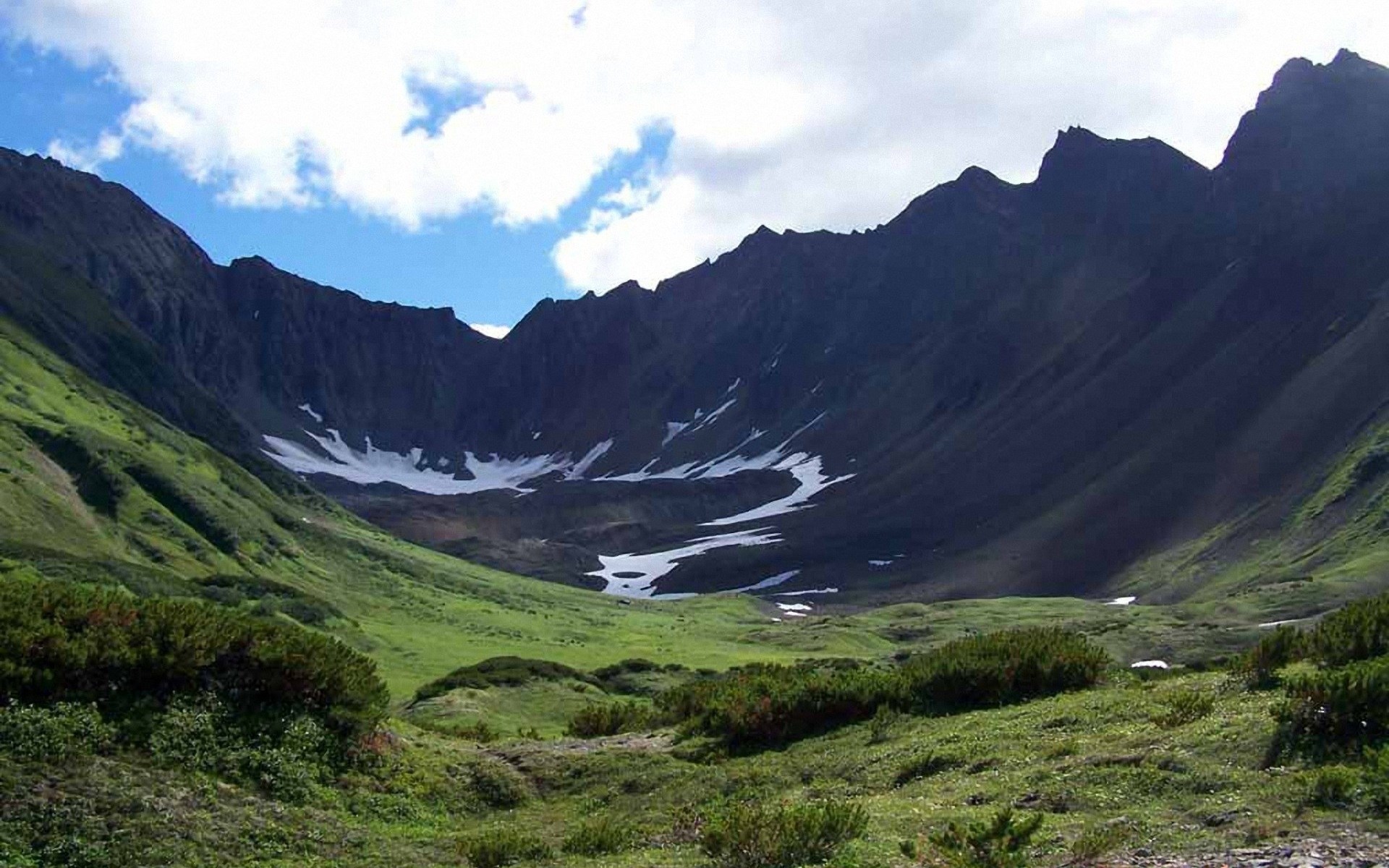 Valley with snow patches and dark mountains HD Wallpaper