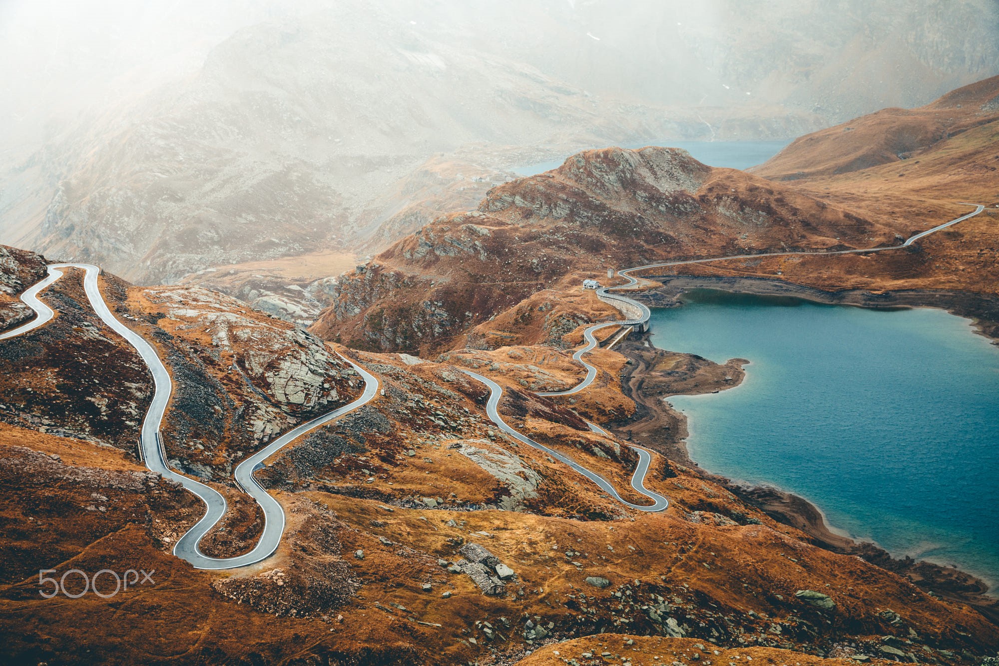 Winding mountain road beside a blue lake HD Wallpaper