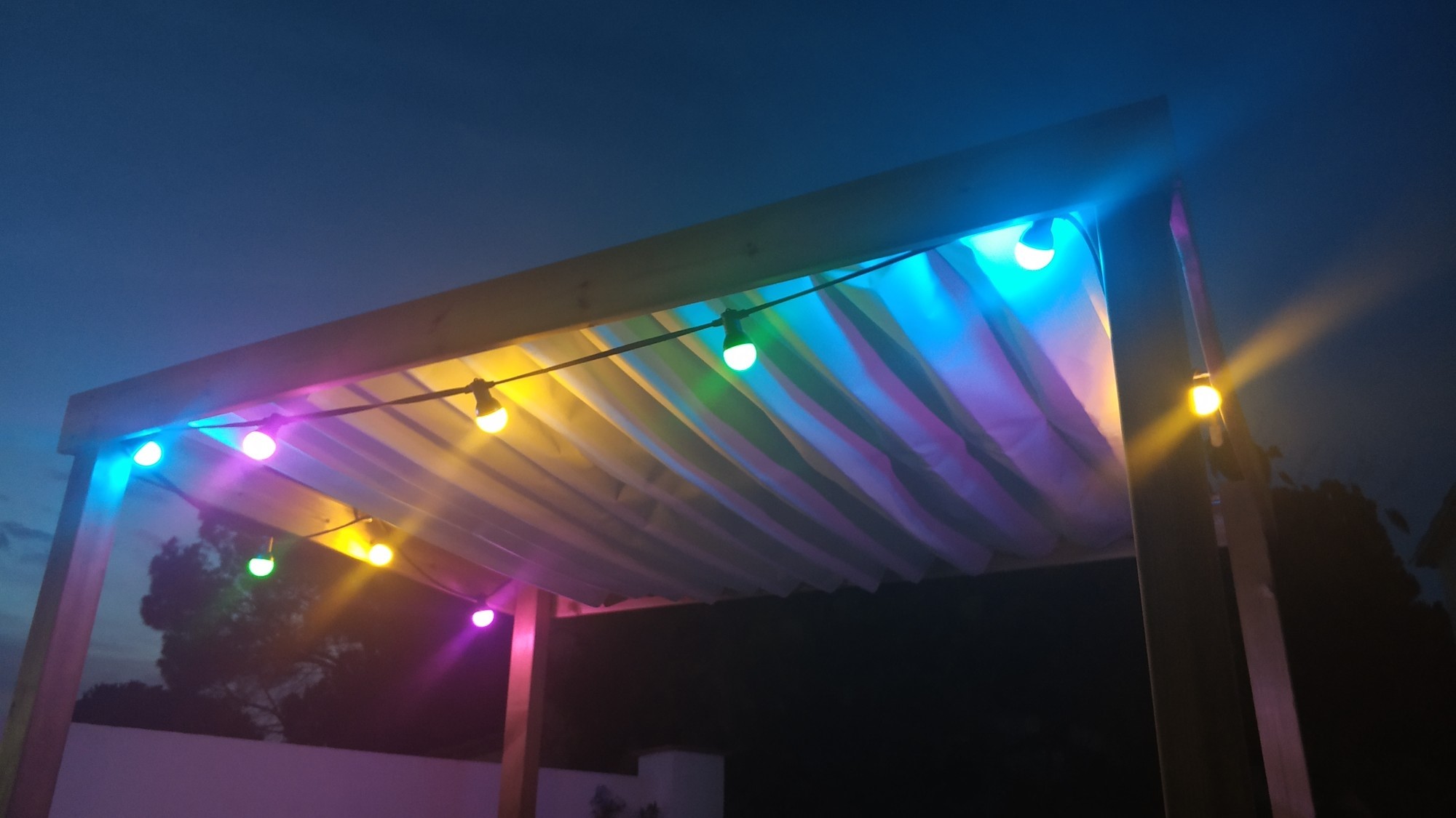 Colorful string lights under a pergola at dusk HD Wallpaper