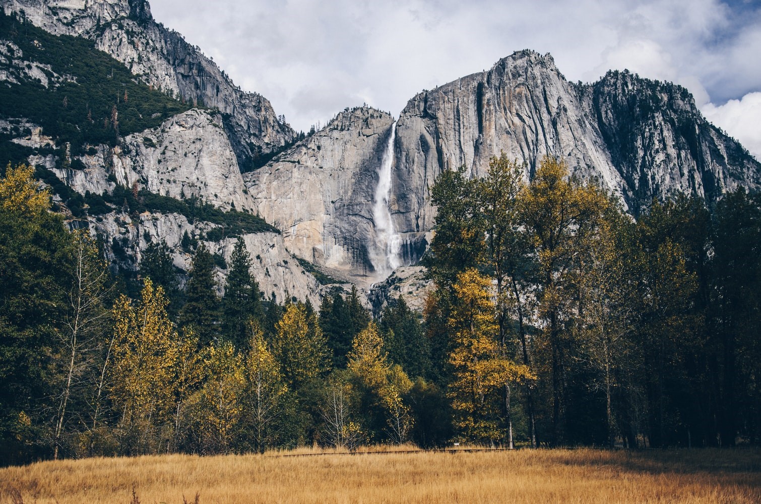 Waterfall cascading down a rocky cliff face with trees in the foreground HD Wallpaper