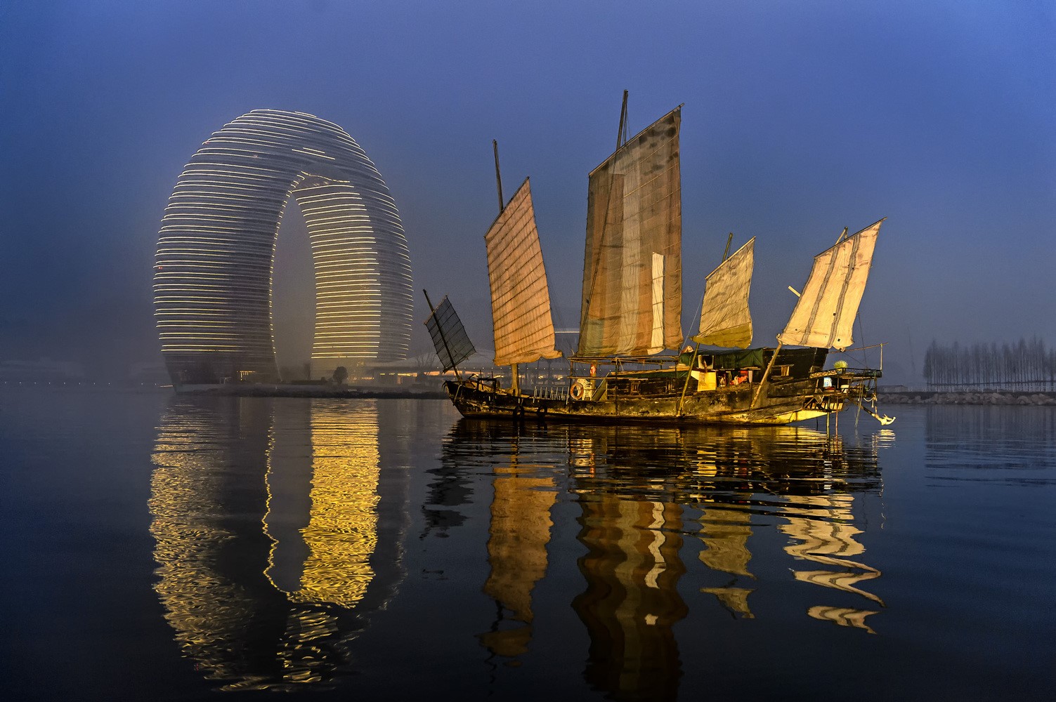 Traditional Chinese junk boat and modern architecture on water at dusk HD Wallpaper