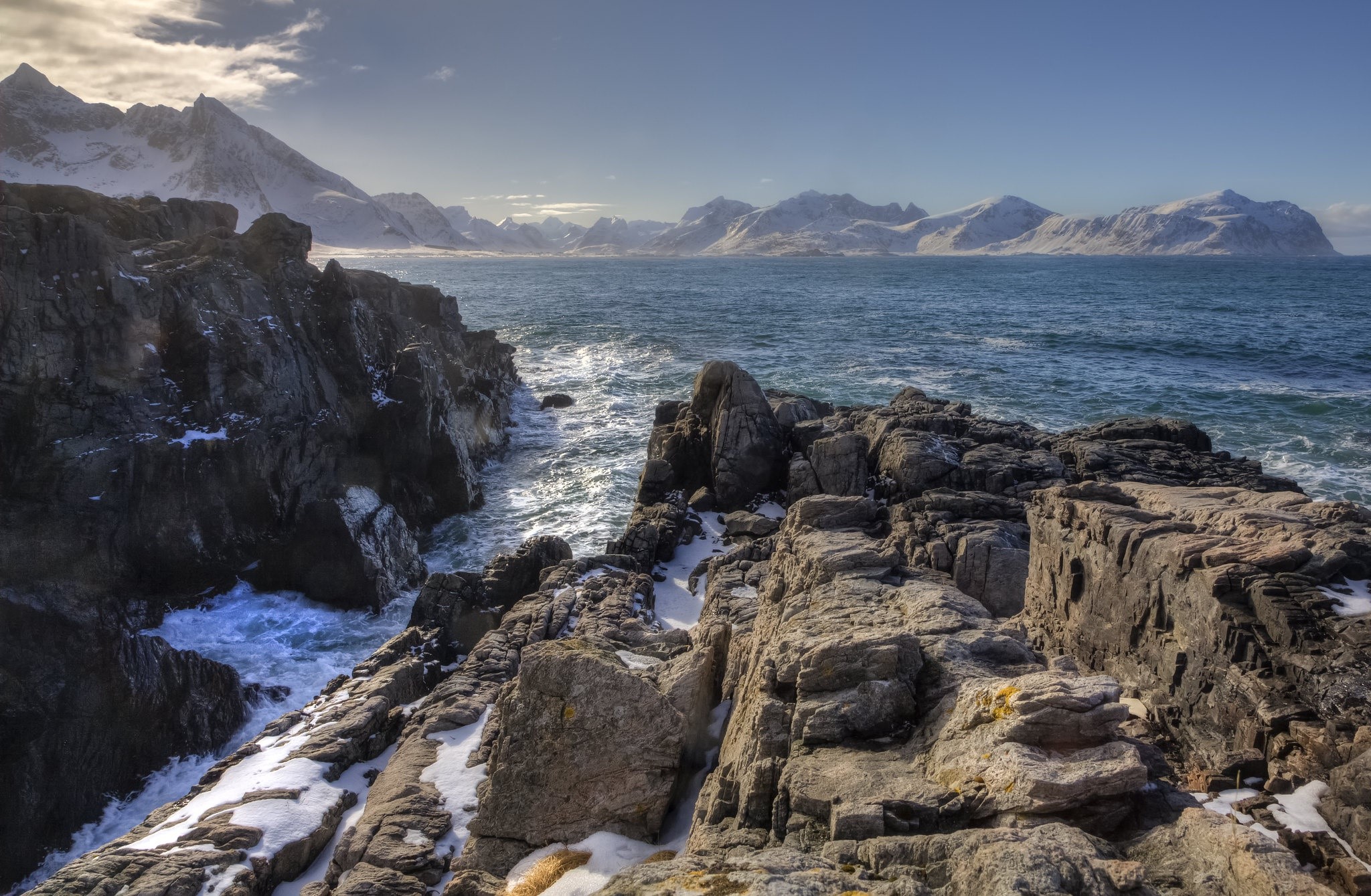 Rocky coastline with snow-capped mountains and sea HD Wallpaper