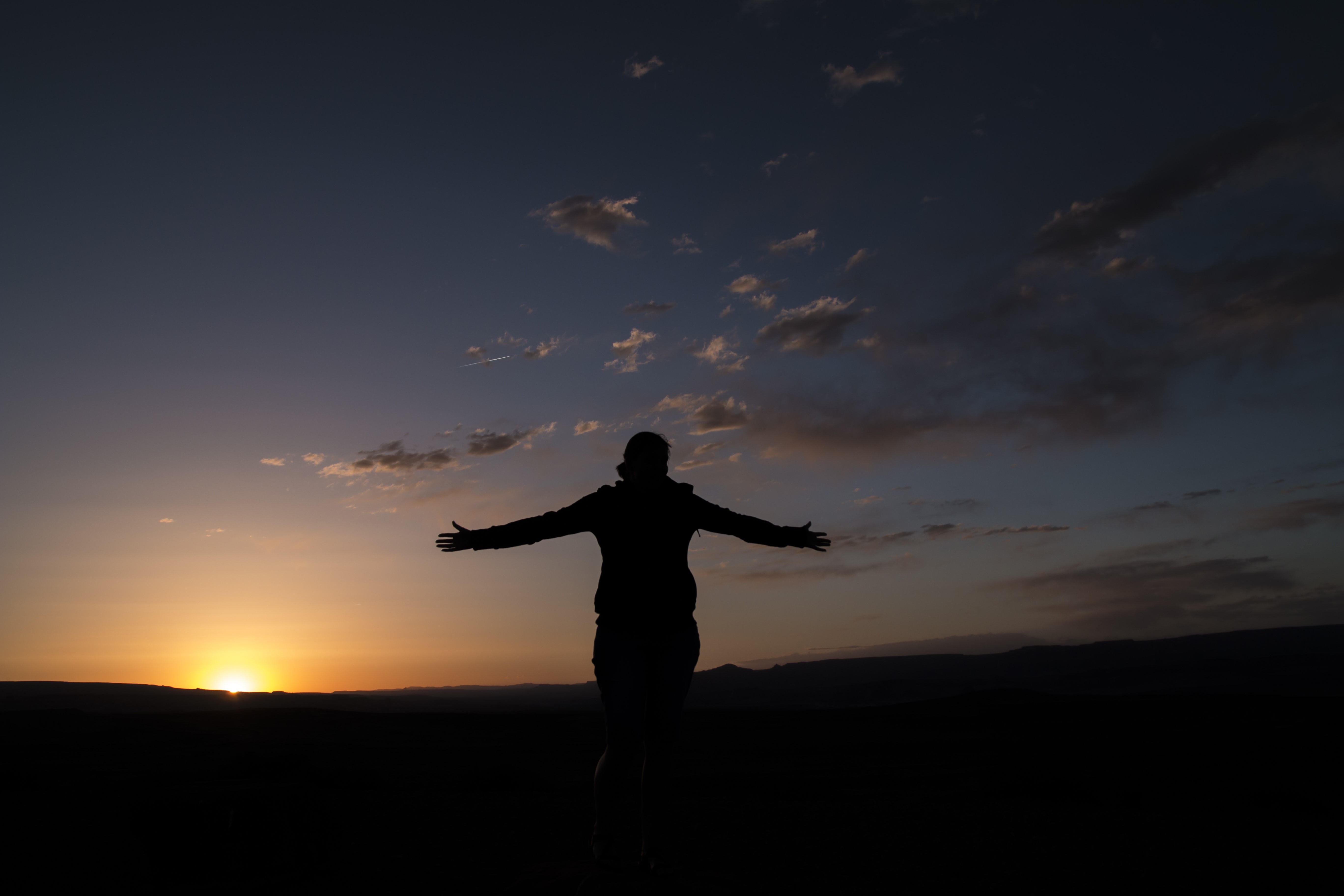 Silhouette of a person with arms outstretched at sunset HD Wallpaper