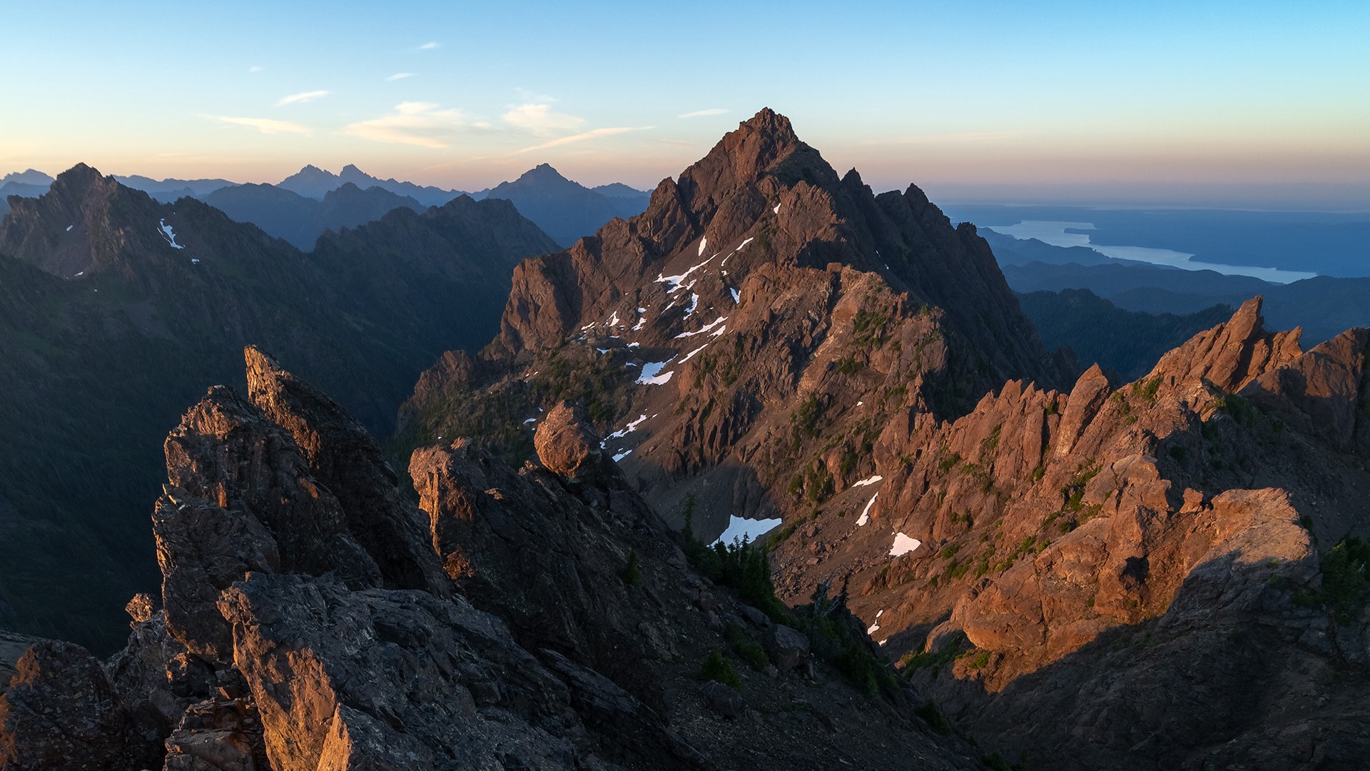 Jagged mountain peaks at sunset with distant water HD Wallpaper