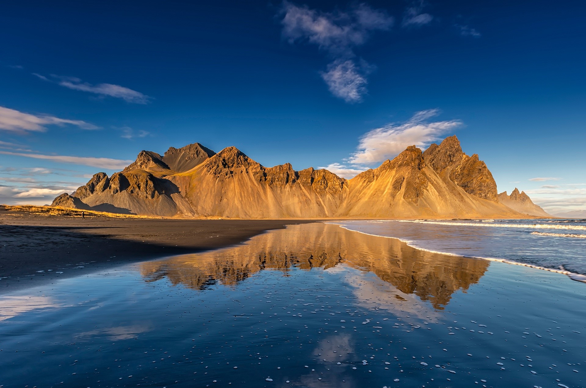 Mountain range reflected in water on a black sand beach HD Wallpaper