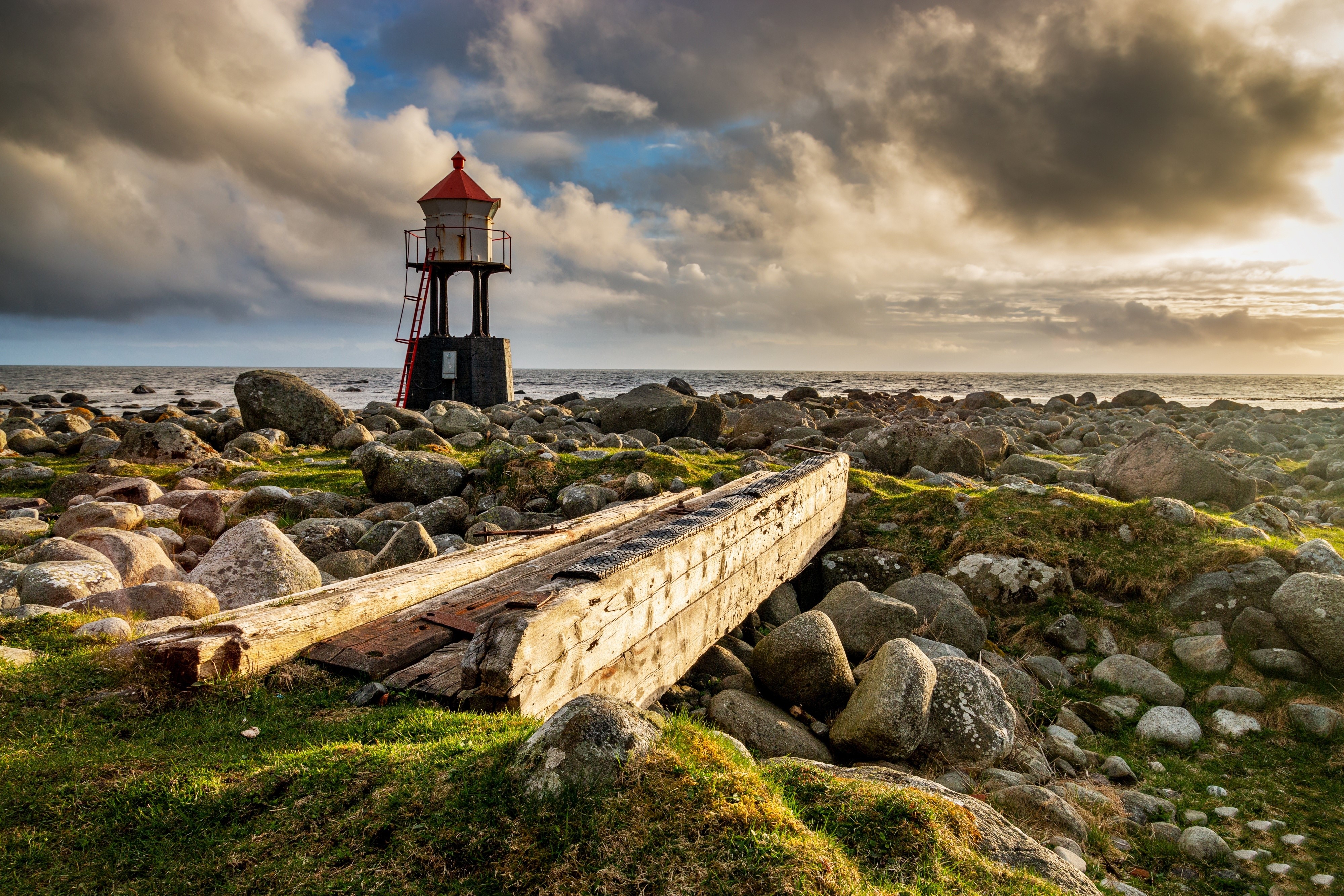 Lighthouse on a rocky coast with a shipwrecked boat HD Wallpaper