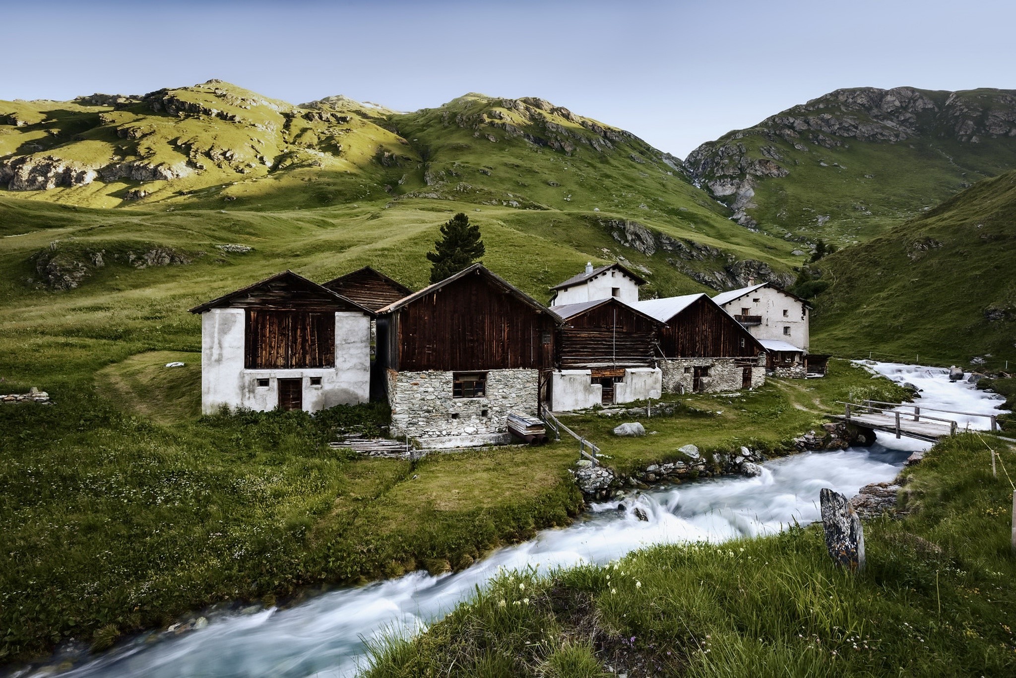 Mountain landscape with old stone and wooden houses by a stream HD Wallpaper