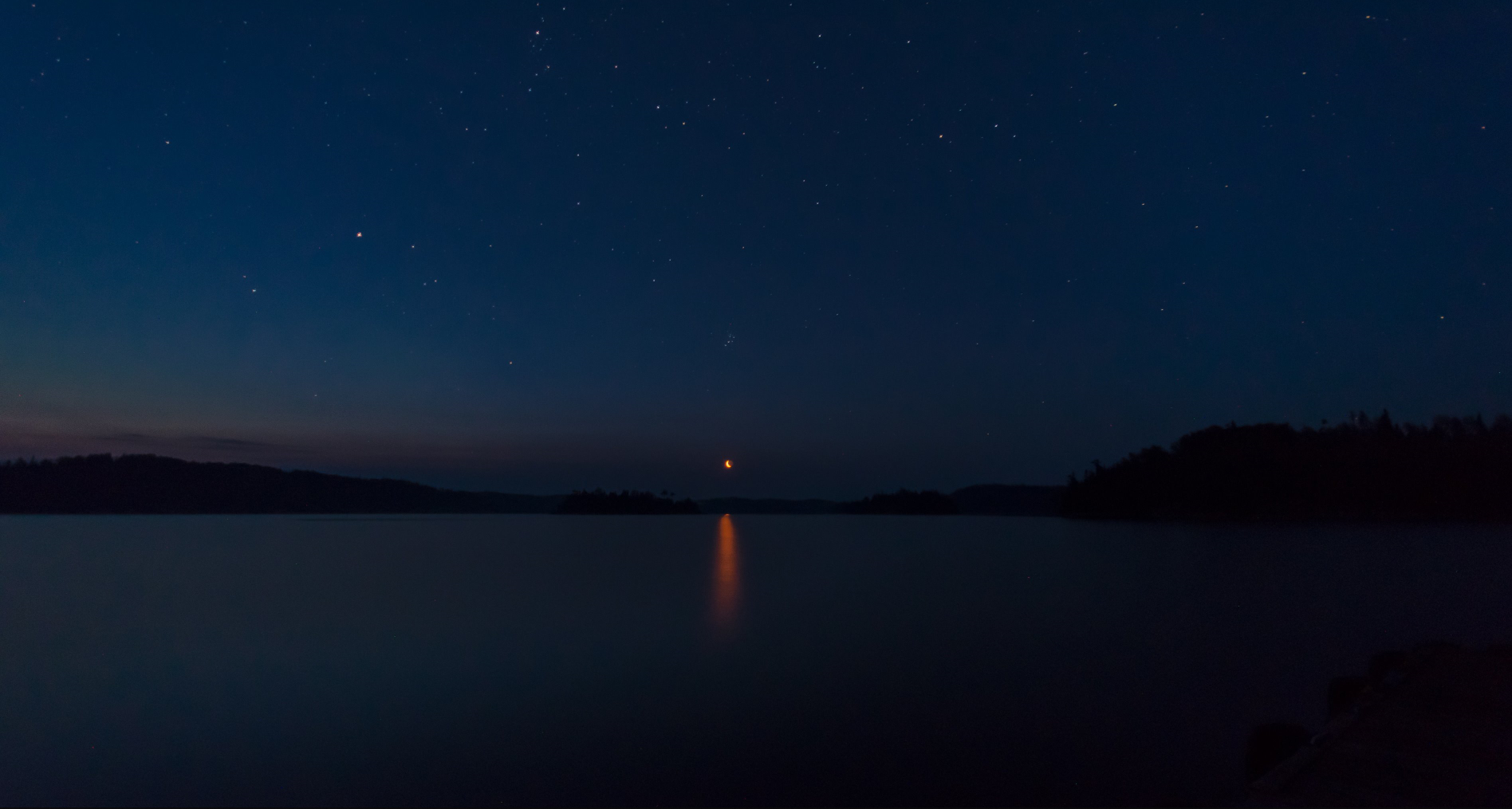 Night sky over a lake with stars and moon reflection HD Wallpaper