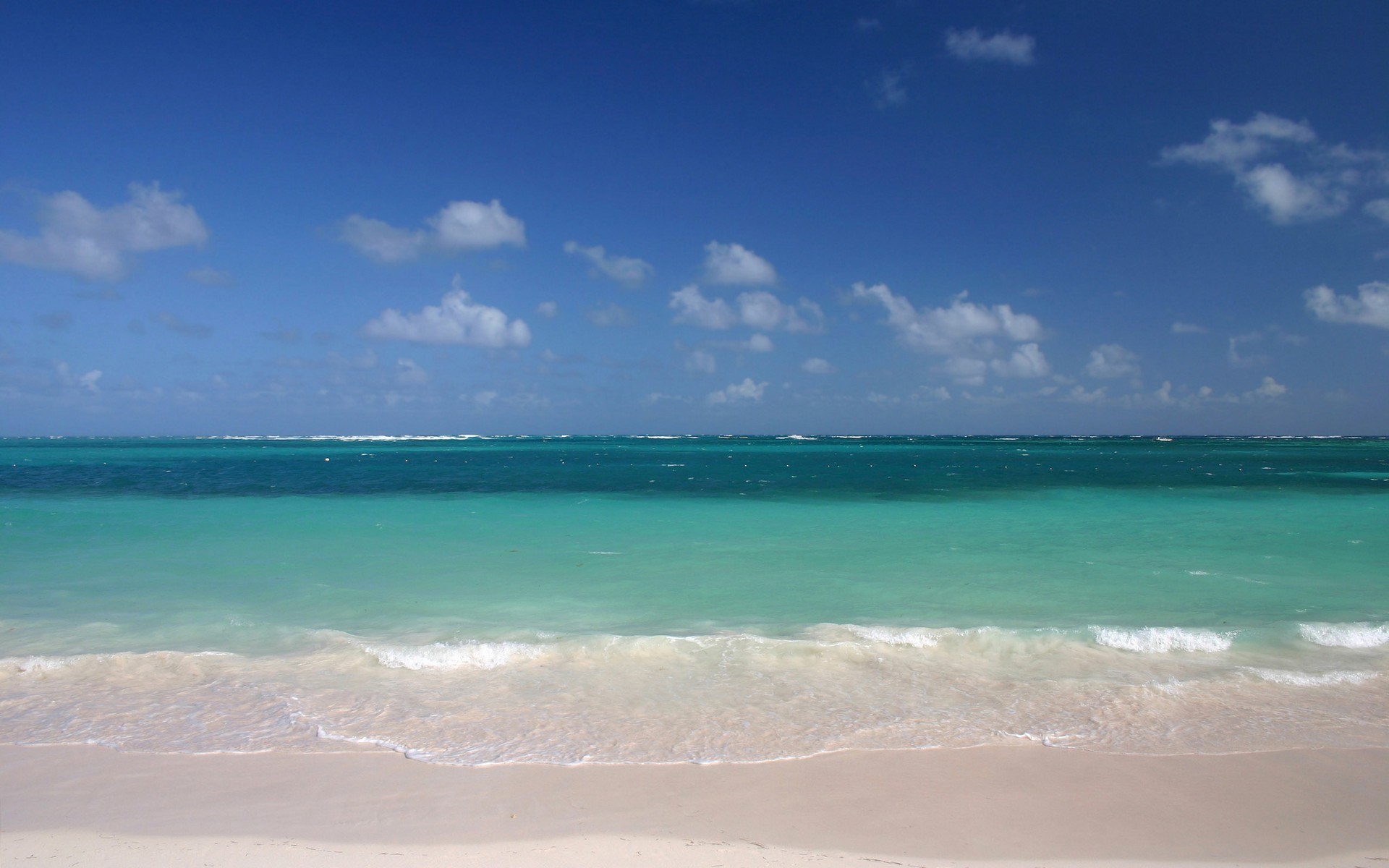Turquoise ocean waves on a sandy beach under a blue sky HD Wallpaper