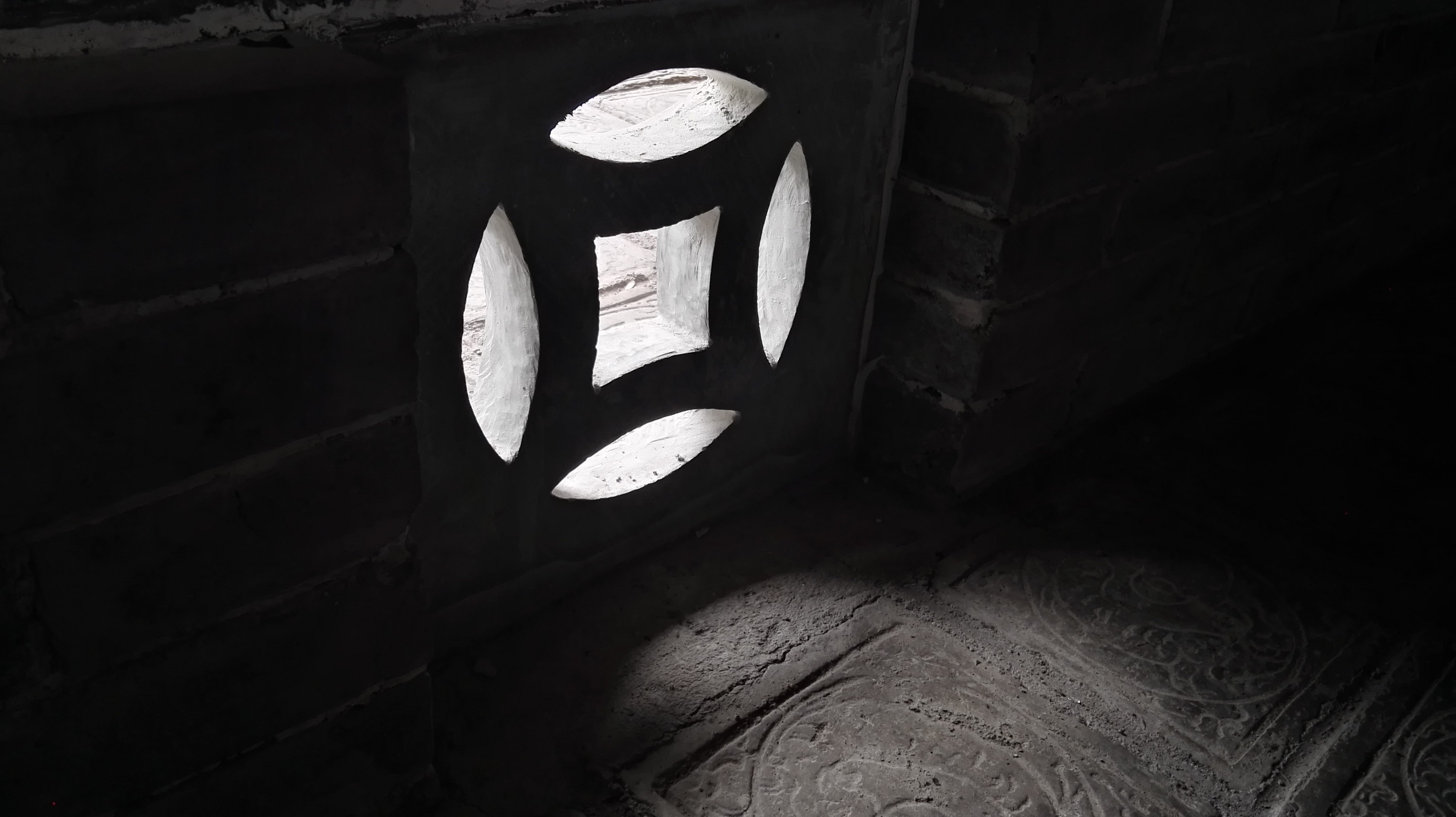 Dark brick wall with light shining through a decorative opening HD Wallpaper