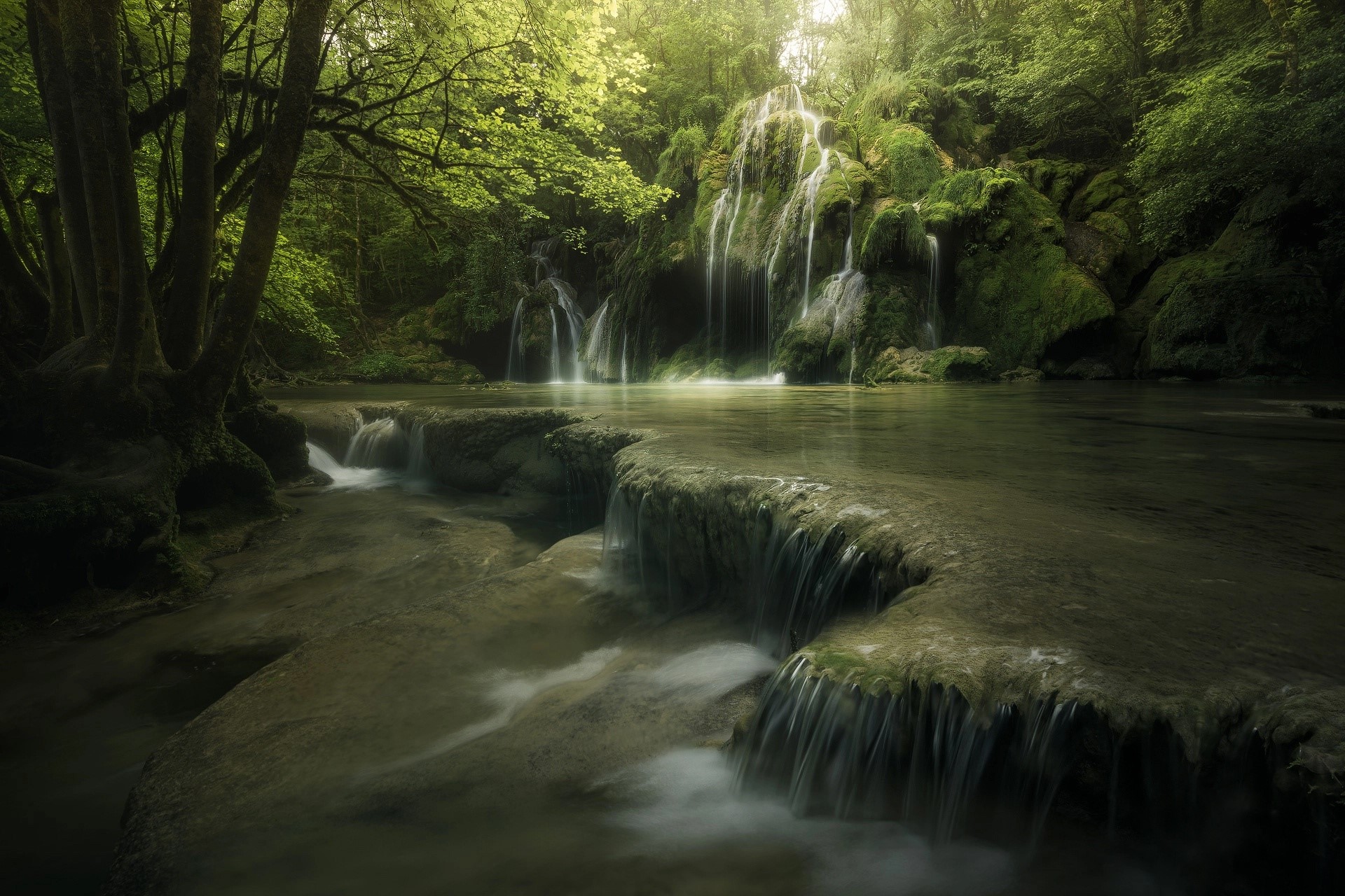 Waterfall cascading over mossy rocks in a lush forest HD Wallpaper