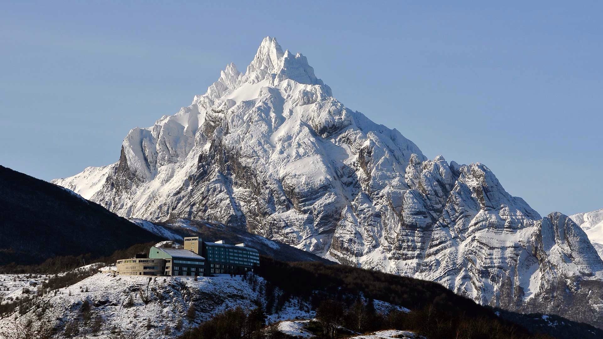 Snowy mountain peak above Ushuaia with a building HD Wallpaper