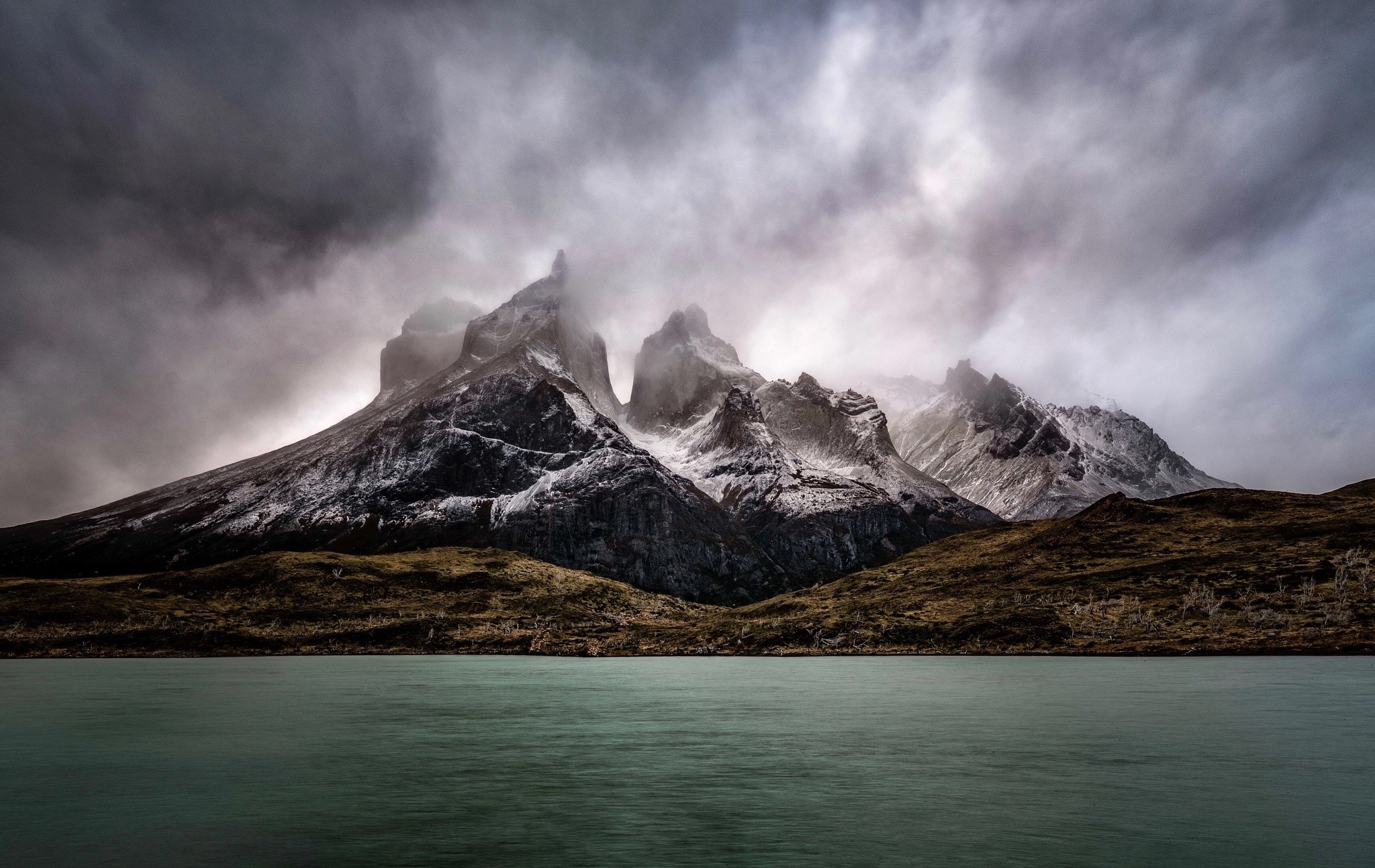 Mountains shrouded in clouds over a lake HD Wallpaper