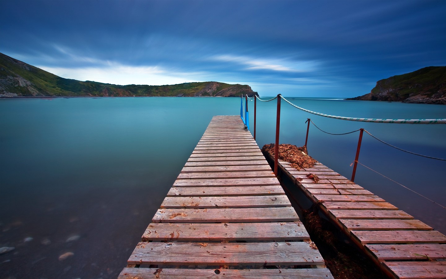 Wooden pier on a calm bay with hills HD Wallpaper