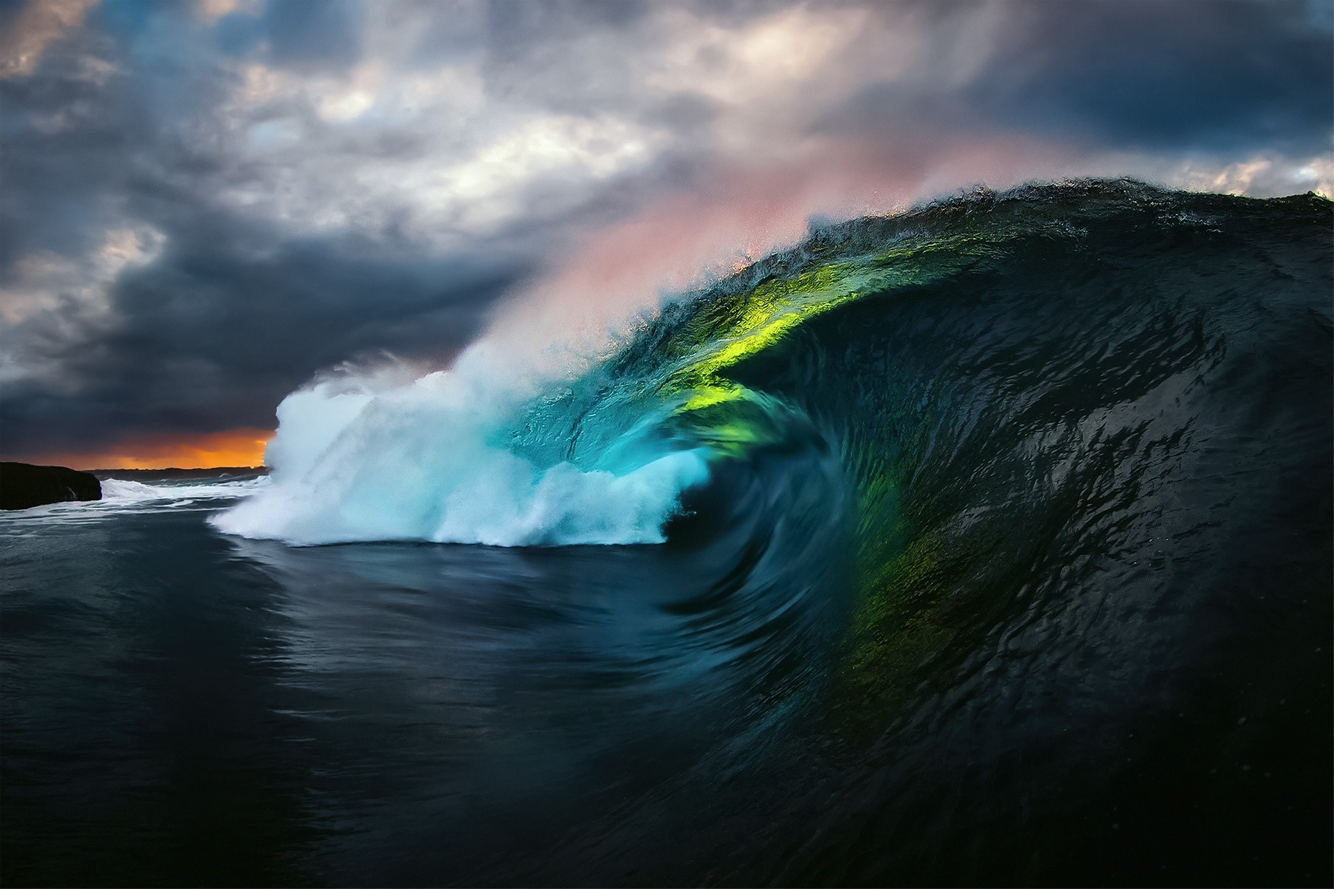 A powerful wave crashes under a stormy sky at sunset HD Wallpaper