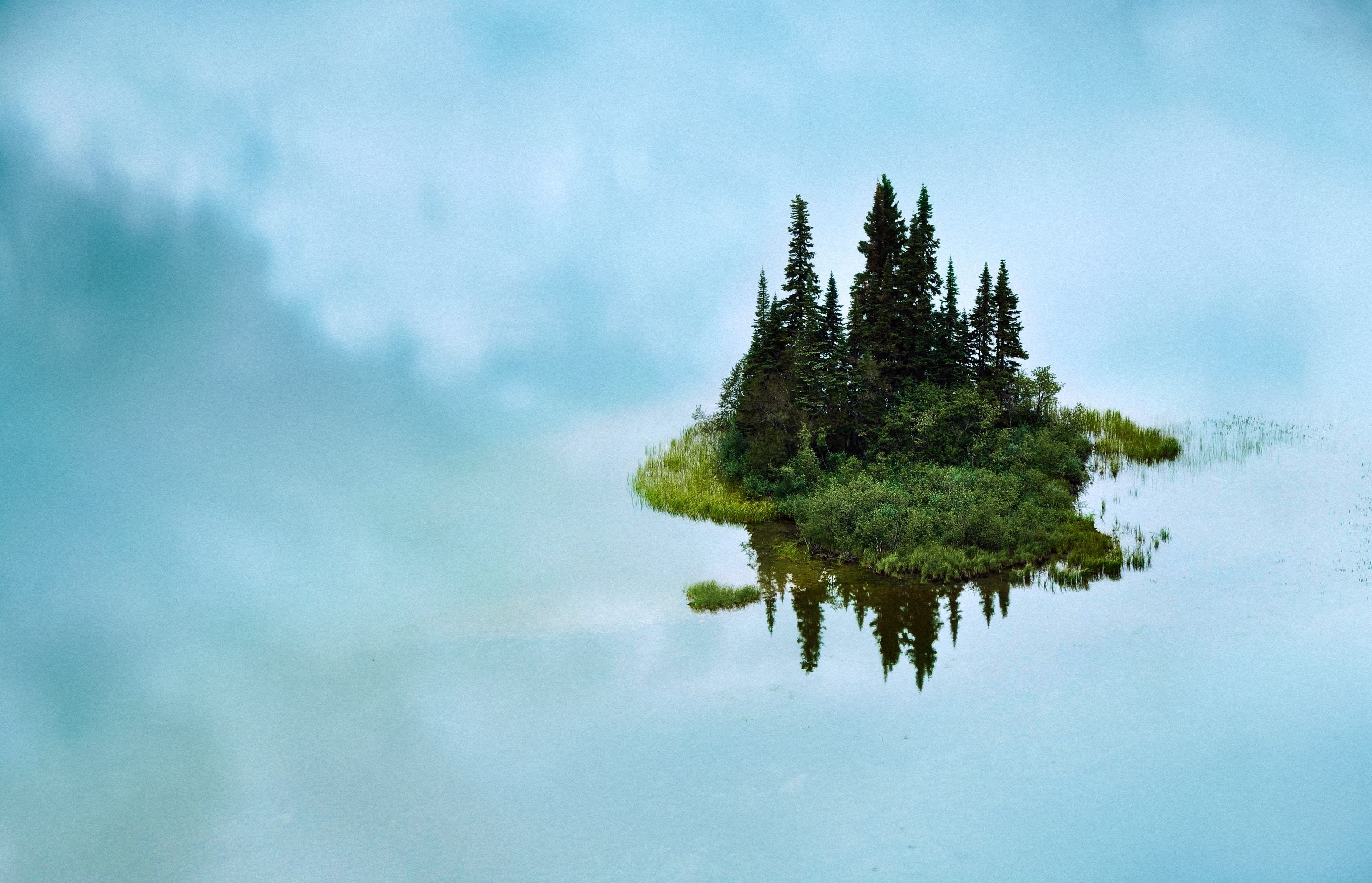 Island with trees reflected in calm water under cloudy sky HD Wallpaper