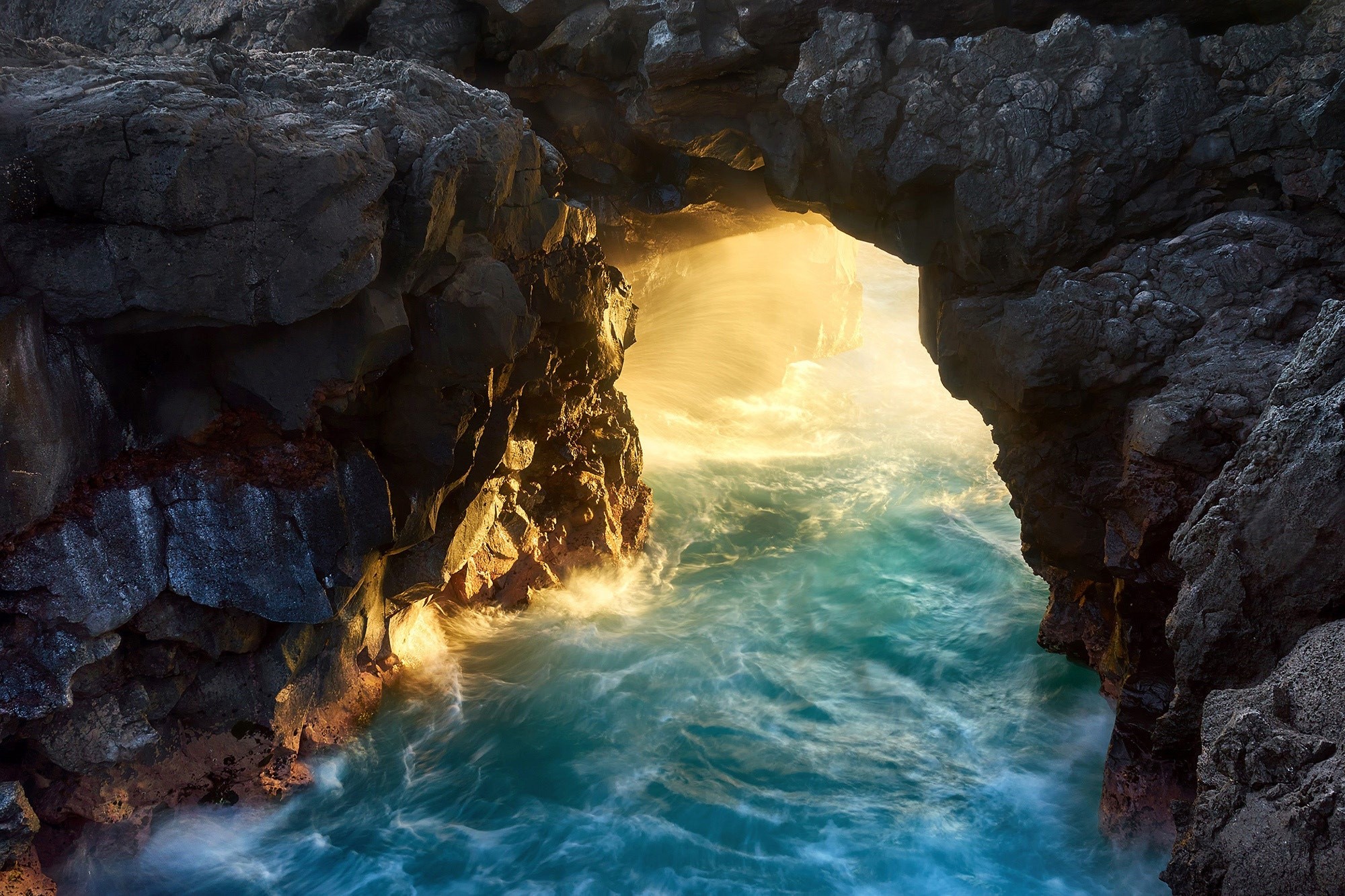 Sunlight shining through a rocky sea cave entrance HD Wallpaper